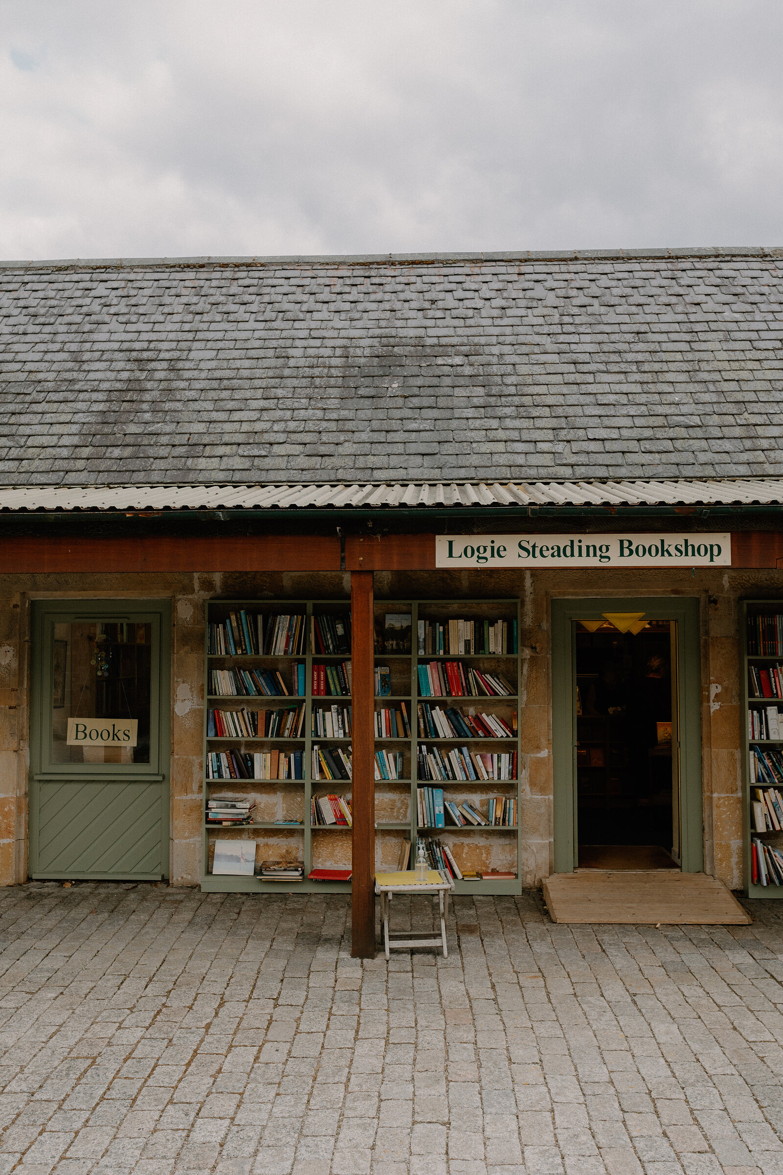 Logie Steading Bookshop's sign hangs above packed shelves and an open door under a stone lintel.