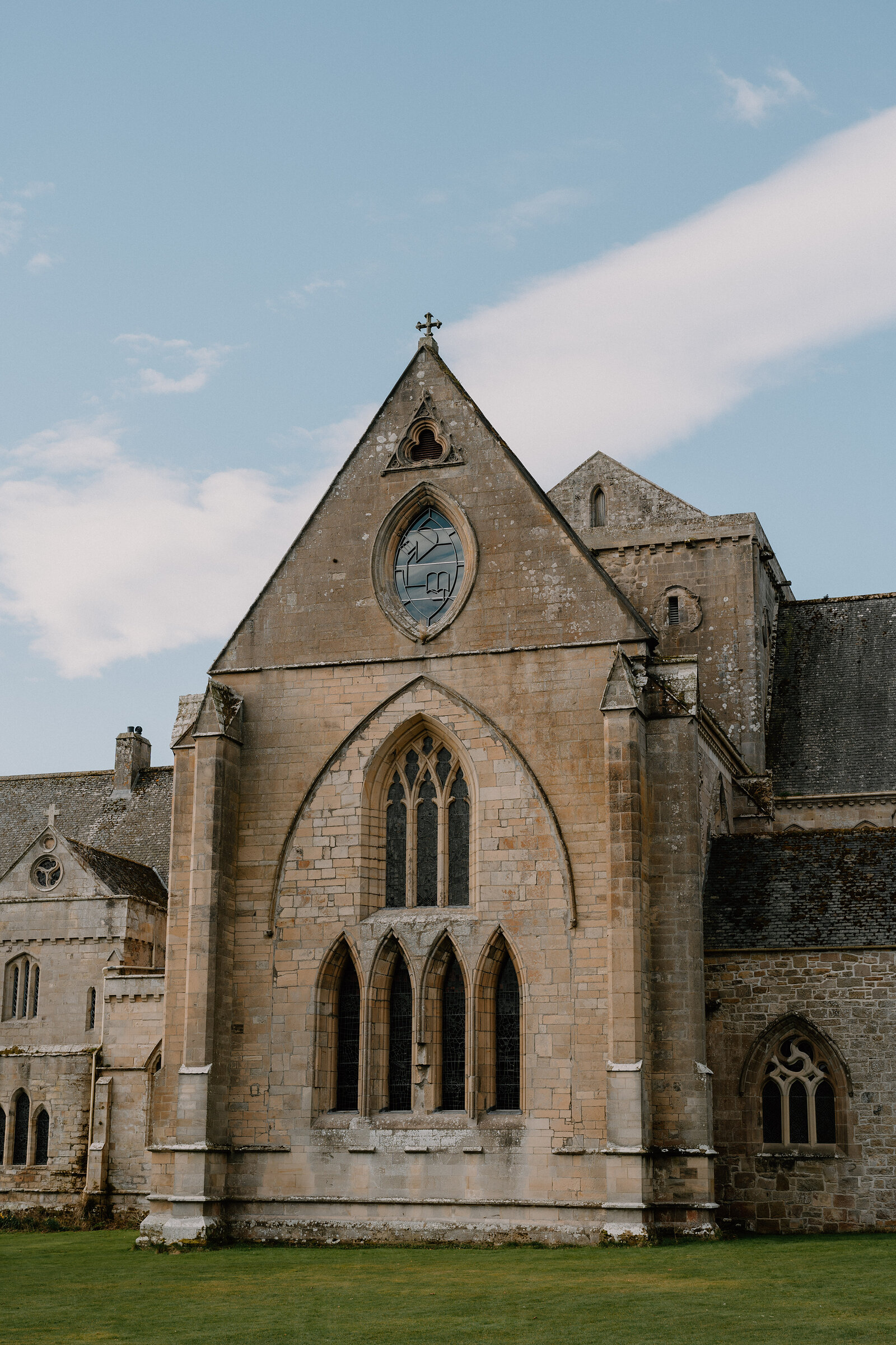 A rose window and stone cross top Pluscarden Abbey's gabled sandstone facade.