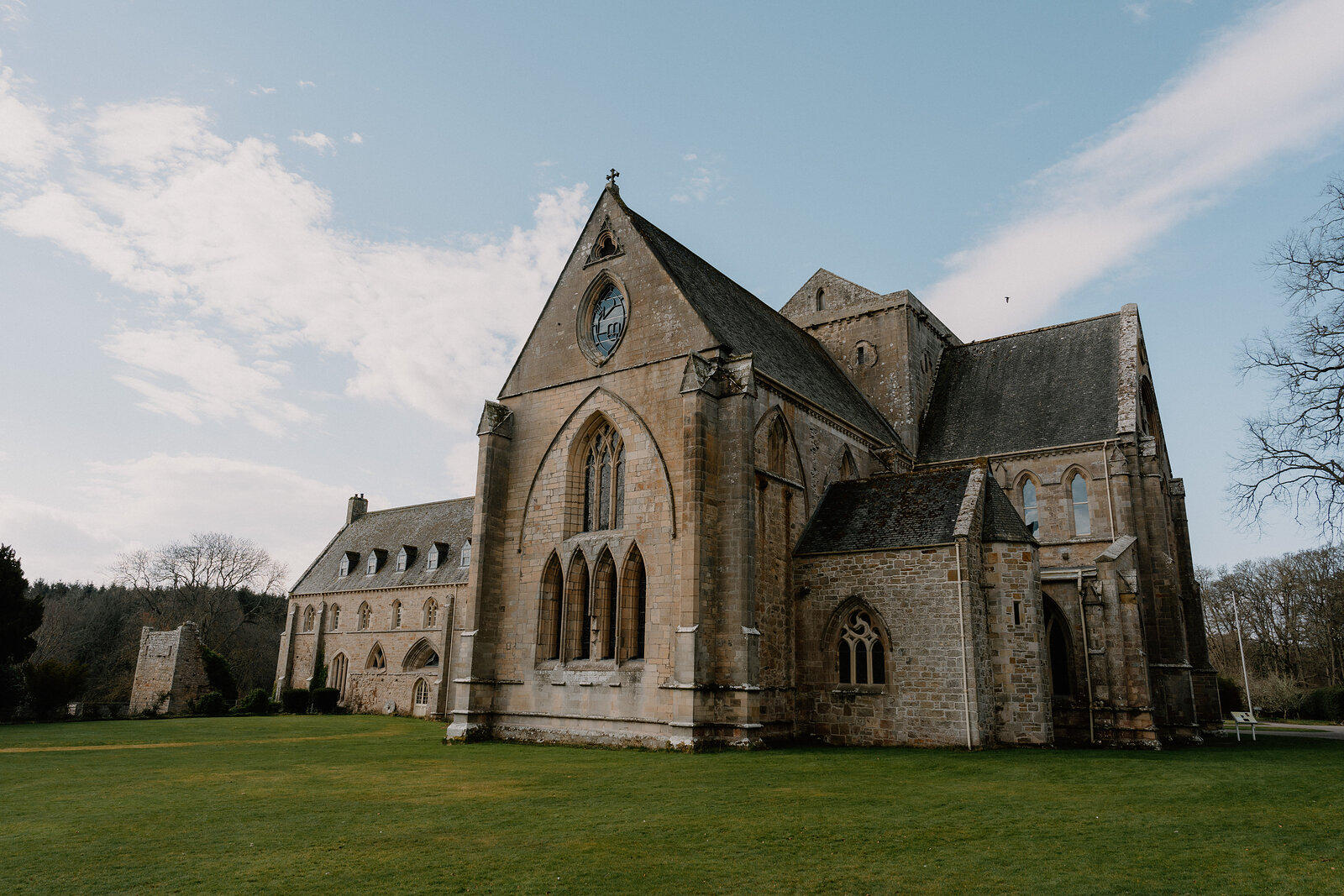 Pluscarden Abbey's long sandstone nave and gabled transept stand on open lawn in Moray.