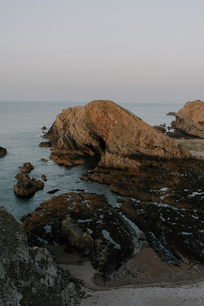 A weathered sandstone arch stands over dark rockpools at the water's edge on the Moray coast.