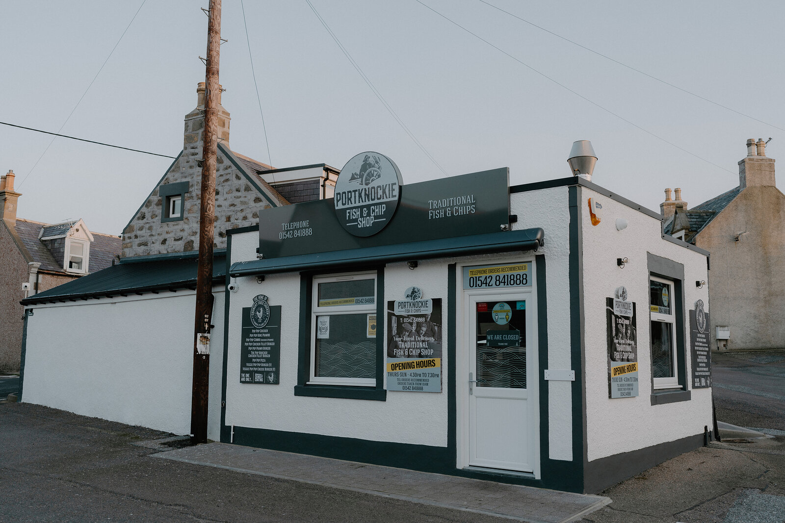 Portknockie Fish & Chip Shop's white frontage sits beneath a wooden telegraph pole on a Moray street.