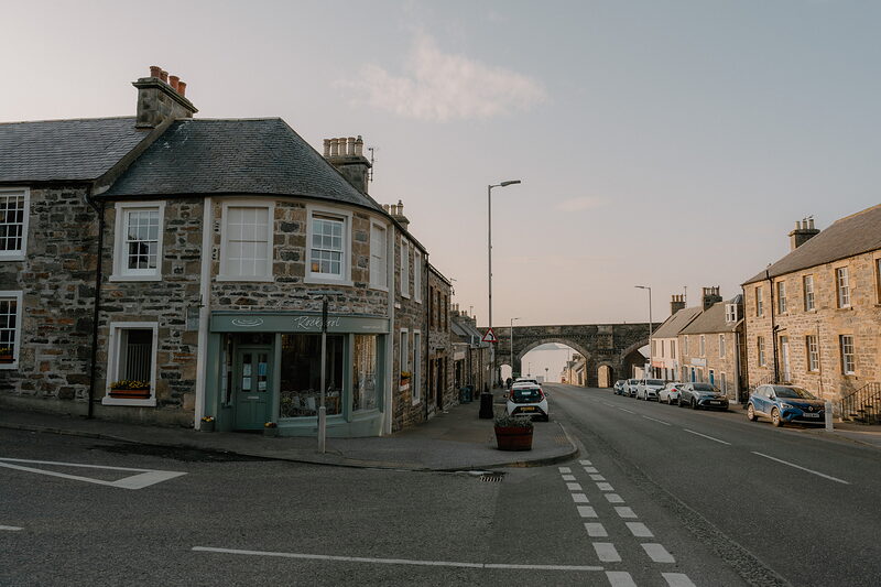 A quiet Cullen street leads toward the town's stone railway viaduct at golden hour.