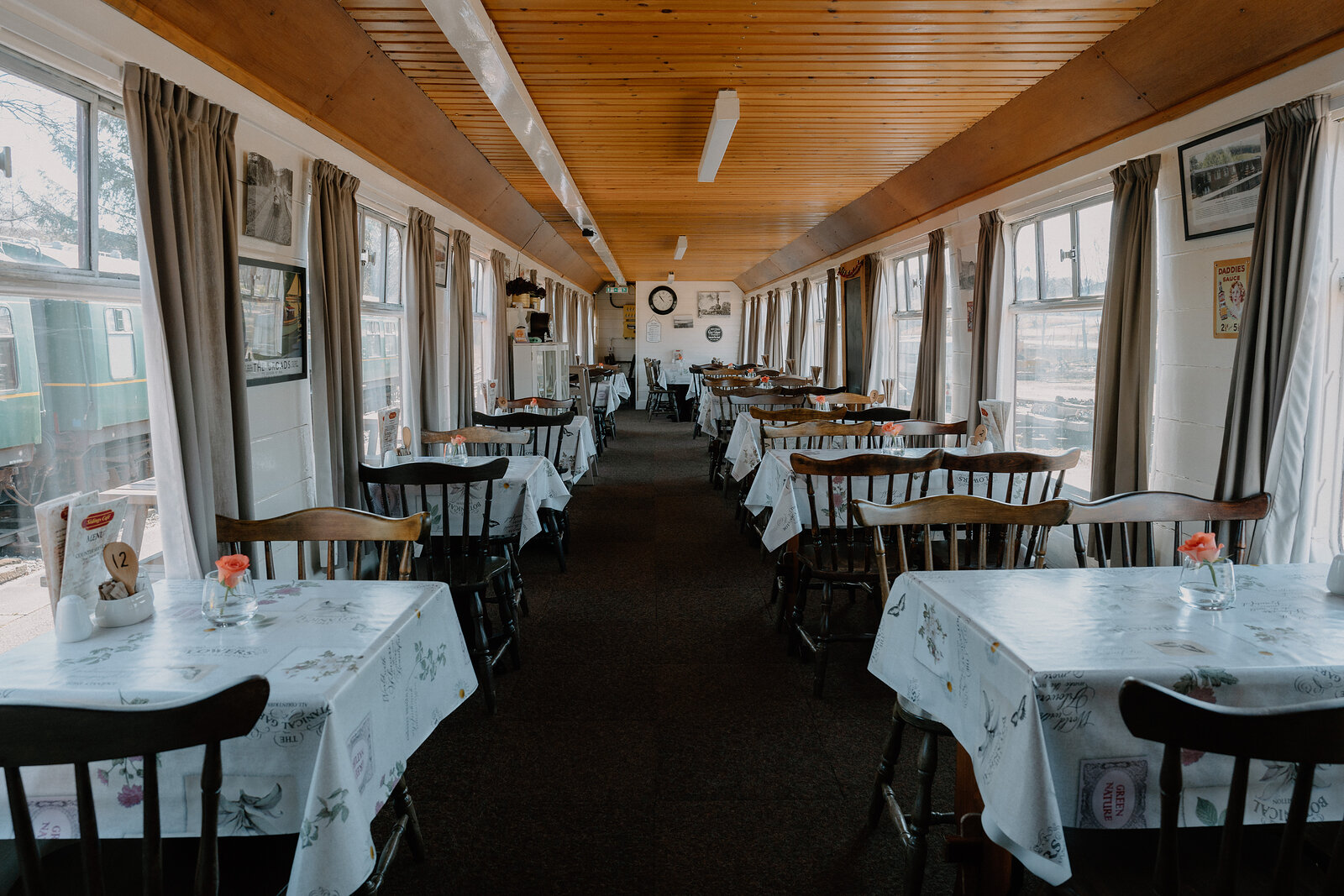 Sidings Café's wood-panelled dining carriage is laid with cloth-covered tables beneath a row of windows.