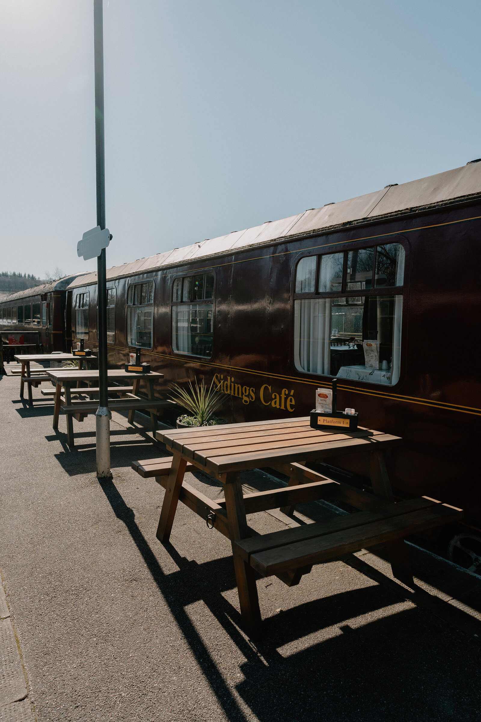 Sidings Café's converted railway carriage stands beside picnic tables in bright sunshine.