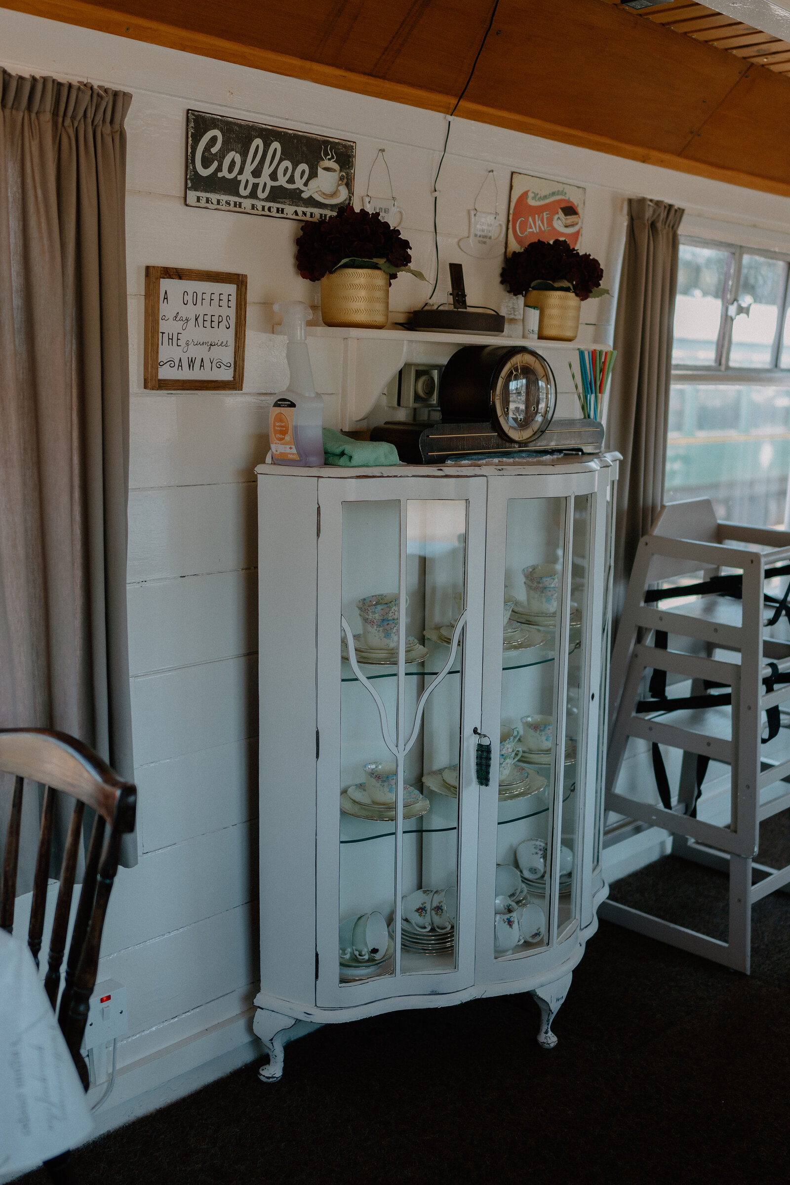 A white display cabinet holds patterned teacups beneath a 'Coffee' sign in Sidings Café.