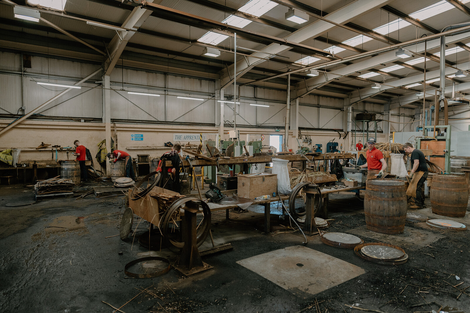 Several workers repair casks on iron jigs across a busy Speyside Cooperage workshop floor.