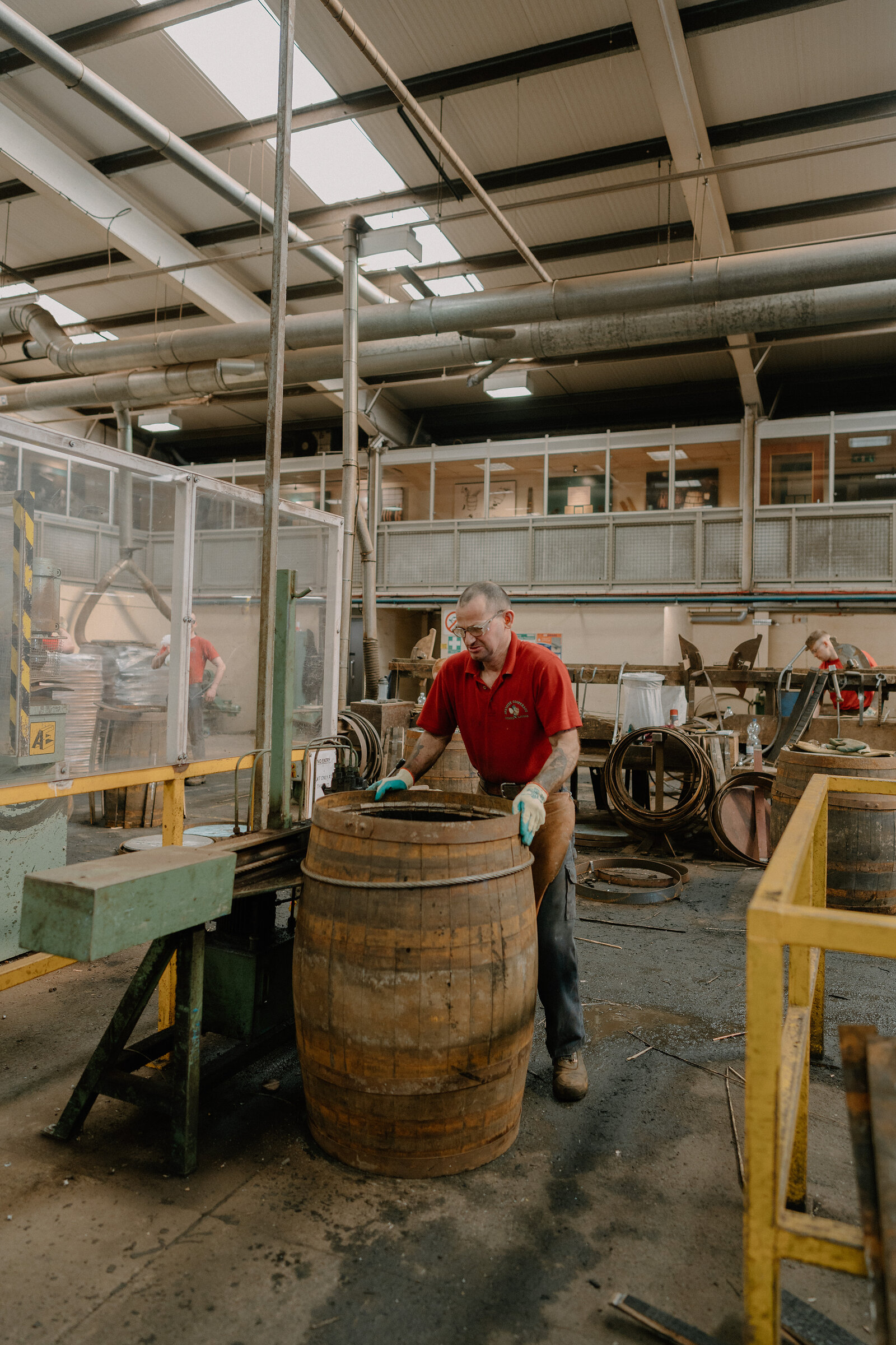 A worker in a red apron fits new hoops onto a cask at Speyside Cooperage.