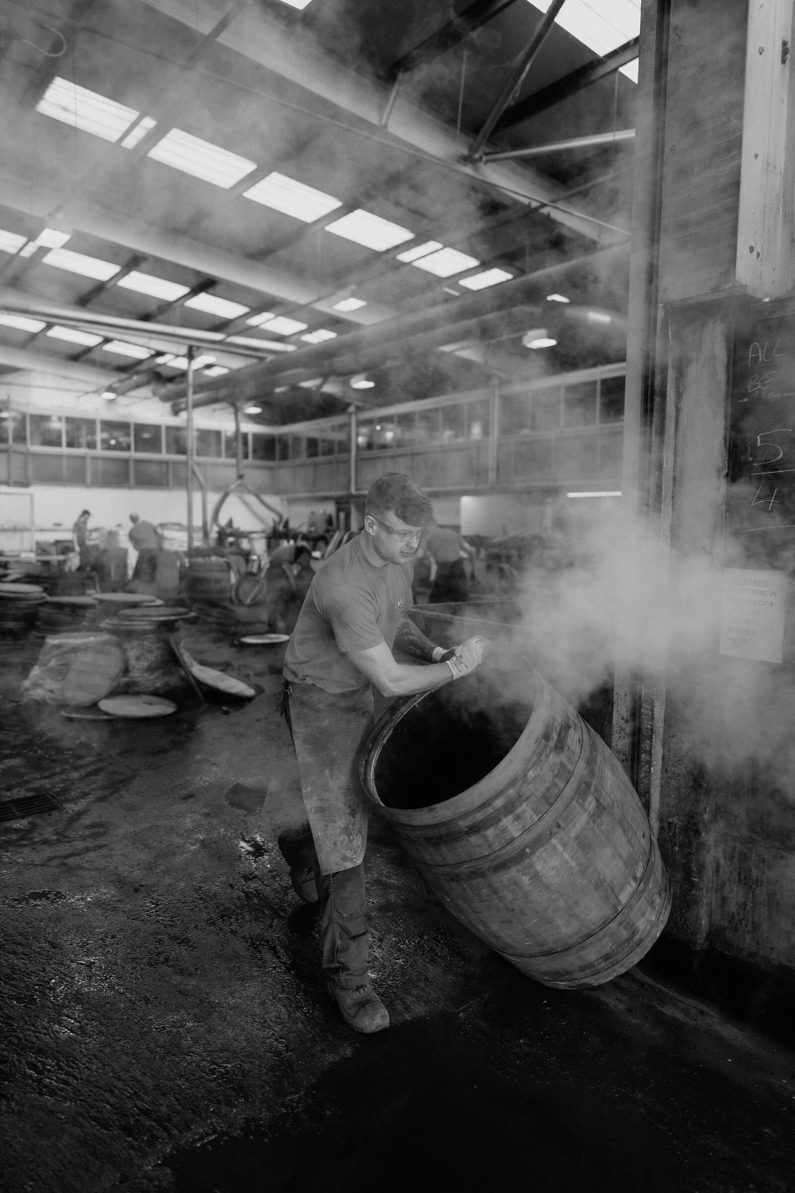 A worker steam-treats a cask amid thick vapour at Speyside Cooperage, rendered in black and white.