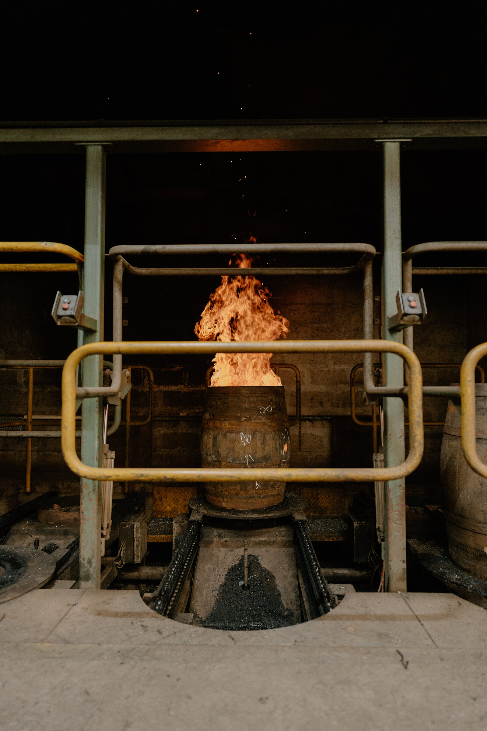 Flames leap from a cask on a charring rig beneath a steel gantry at Speyside Cooperage.