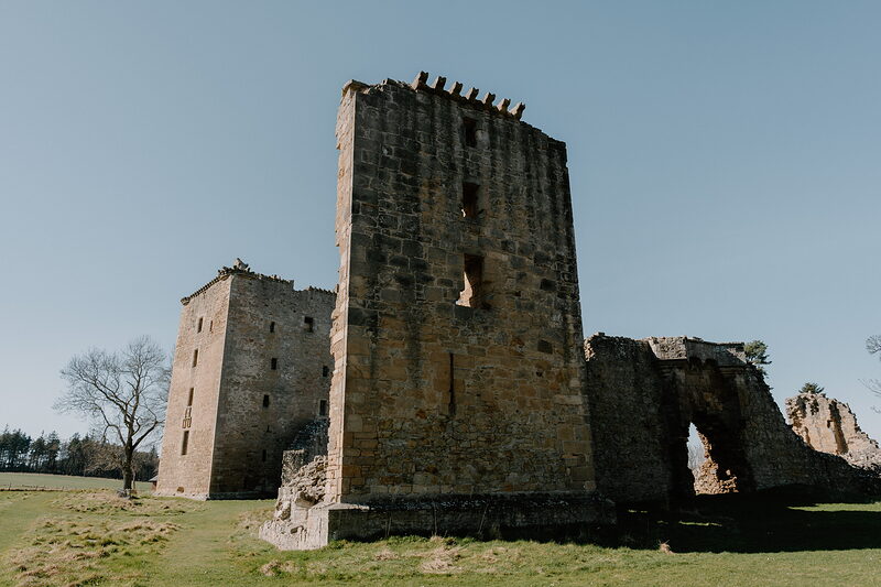 Spynie Palace's great tower stands beside a smaller ruined wing on open parkland.