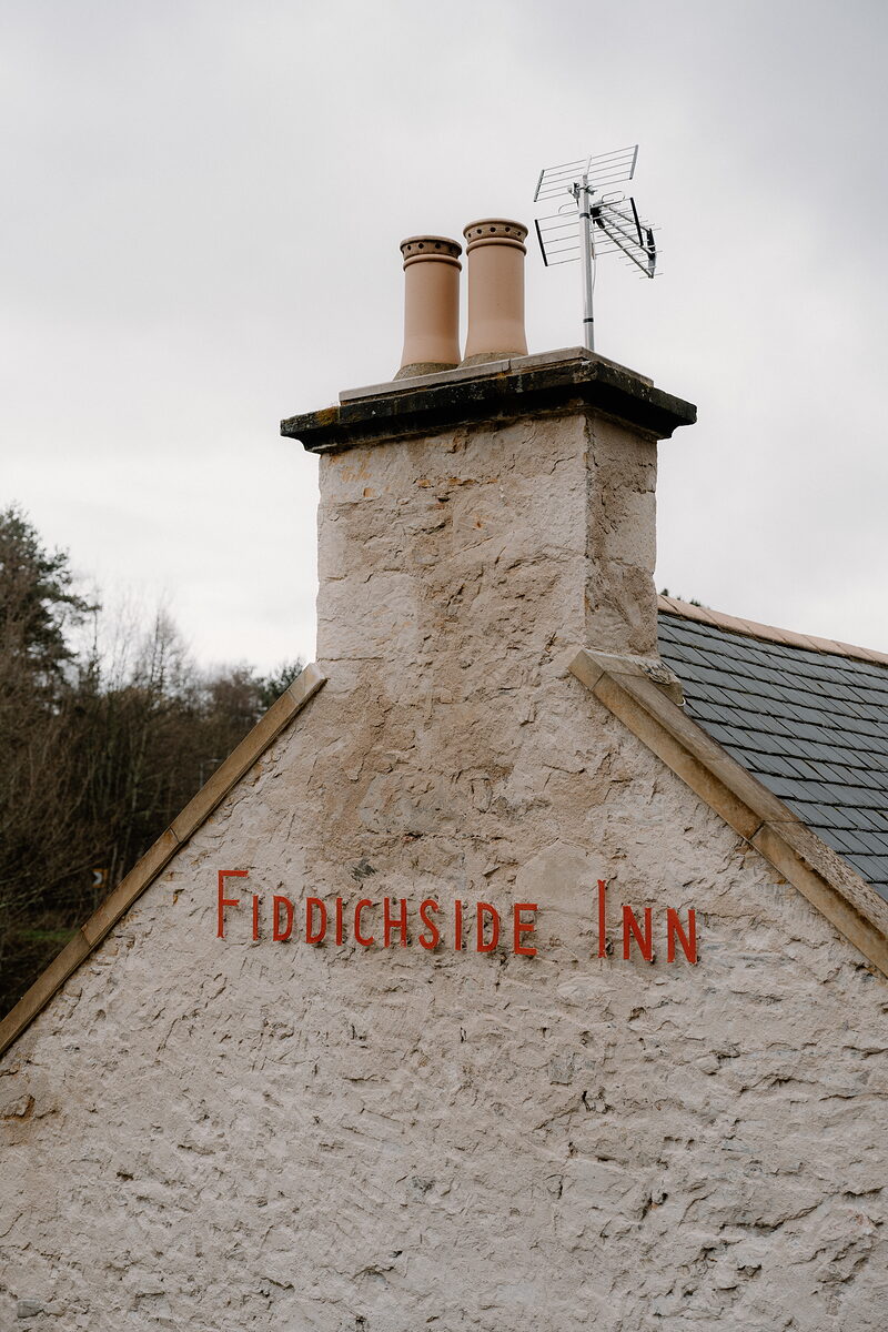 The Fiddichside Inn's name is painted in red across its whitewashed chimney gable.