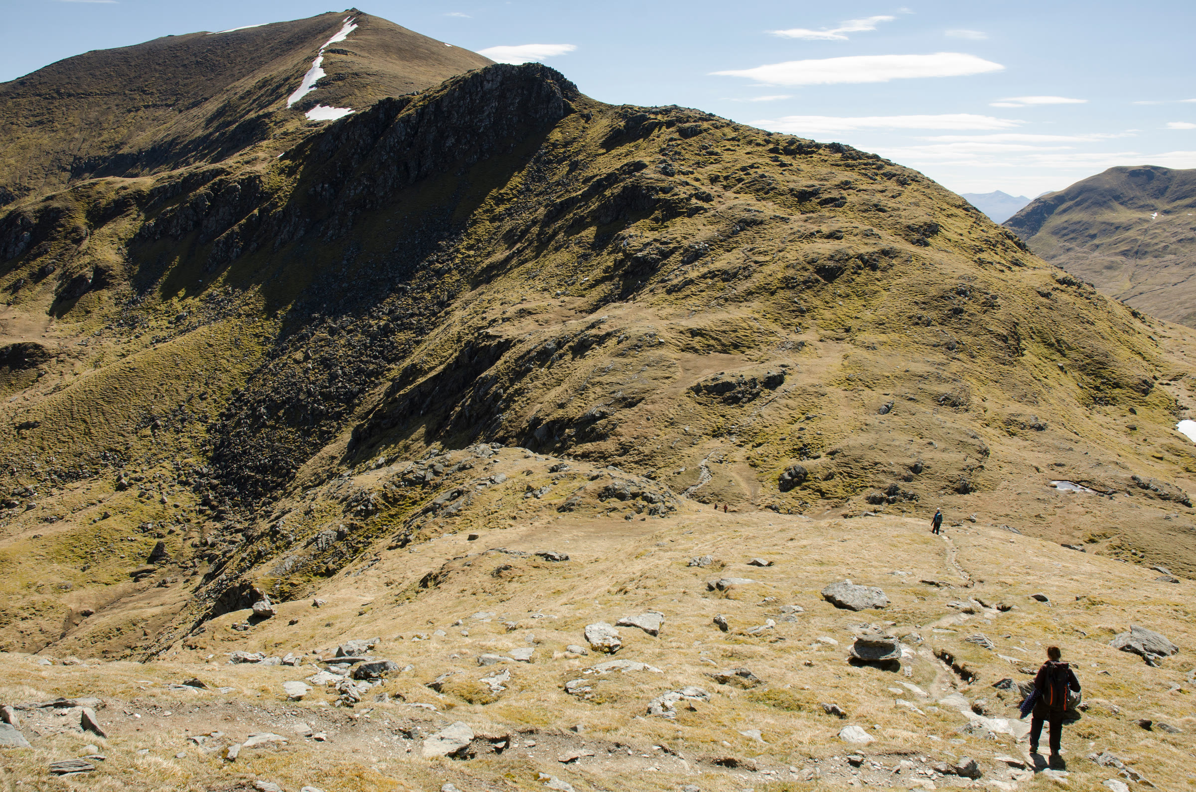 The steep, craggy face of An Stuc on the Ben Lawers ridge, a walker small on the grass below.