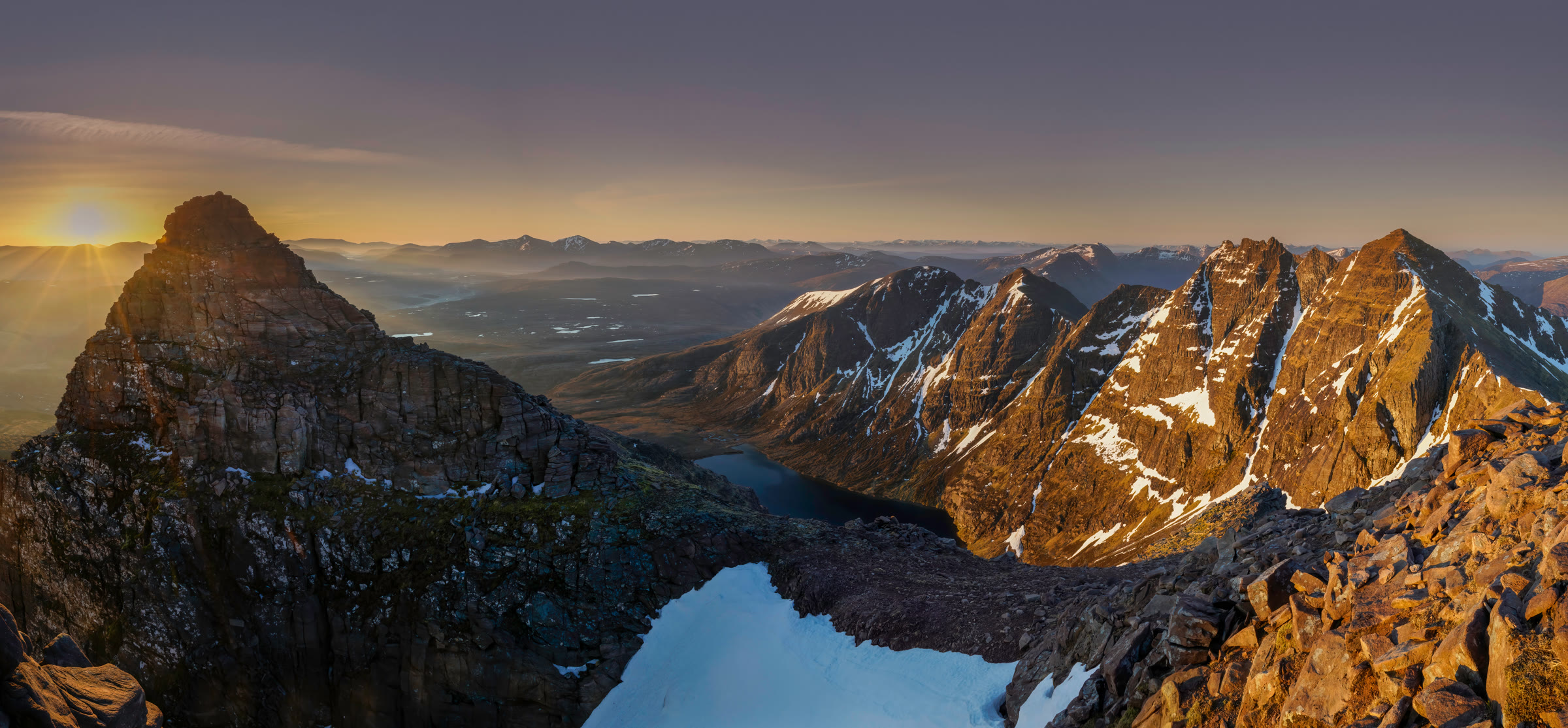 An Teallach at sunrise, its pinnacled ridge lit gold above a snow-filled gully and a dark loch.