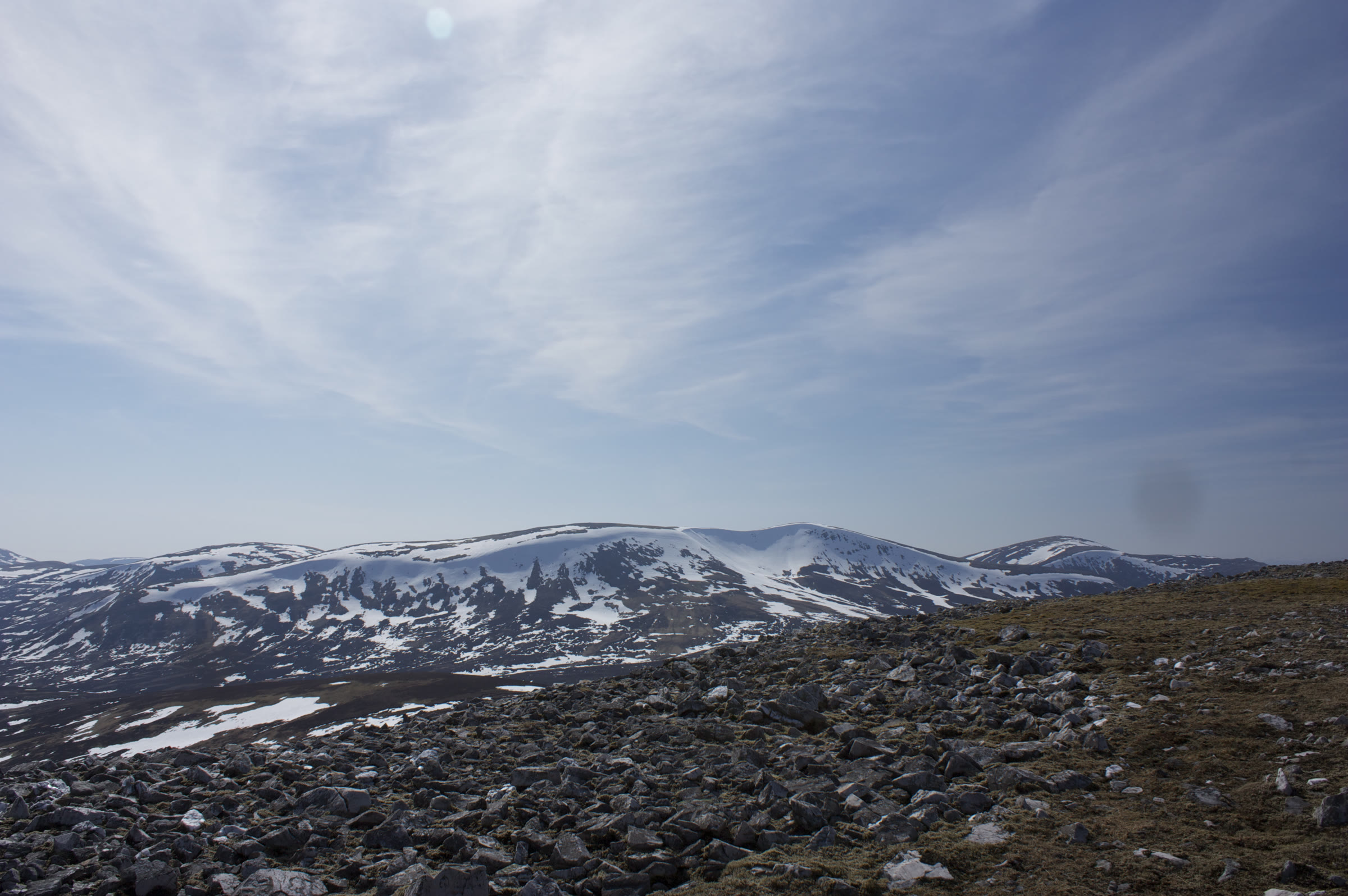 A wide sky of high cloud over Beinn Iutharn Mhòr, streaked with snow, beyond a field of boulders.