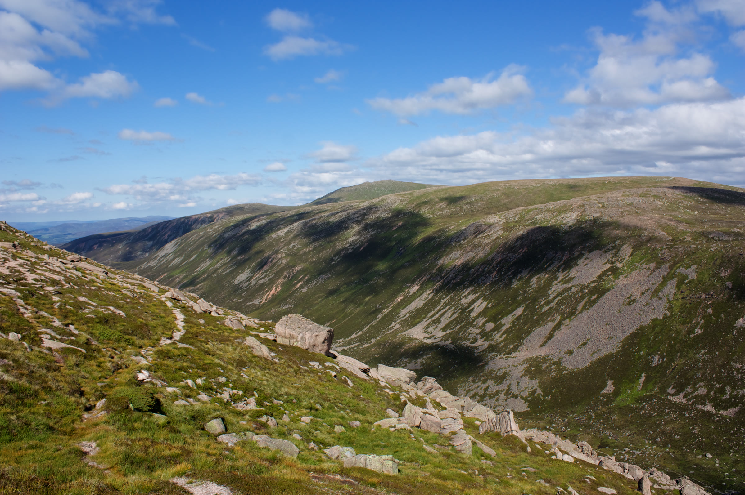 Bynack More in sunshine above Strath Nethy, a path crossing the boulder-strewn slope in front.
