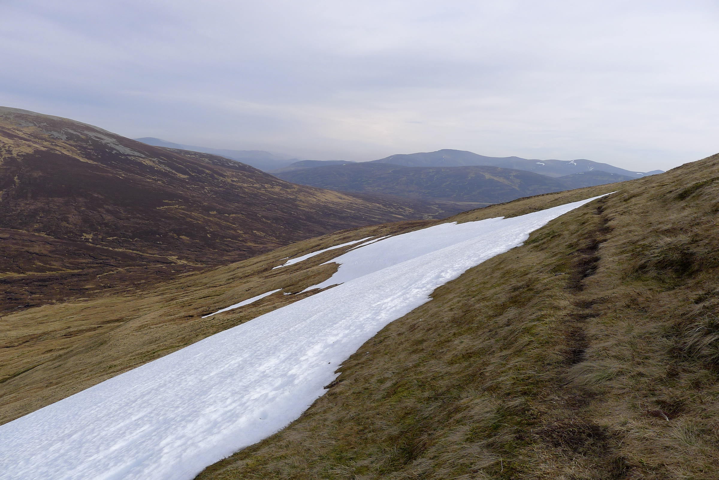A late snow patch beside the faint path on Càrn an Fhìdhleir, with brown hills beyond.