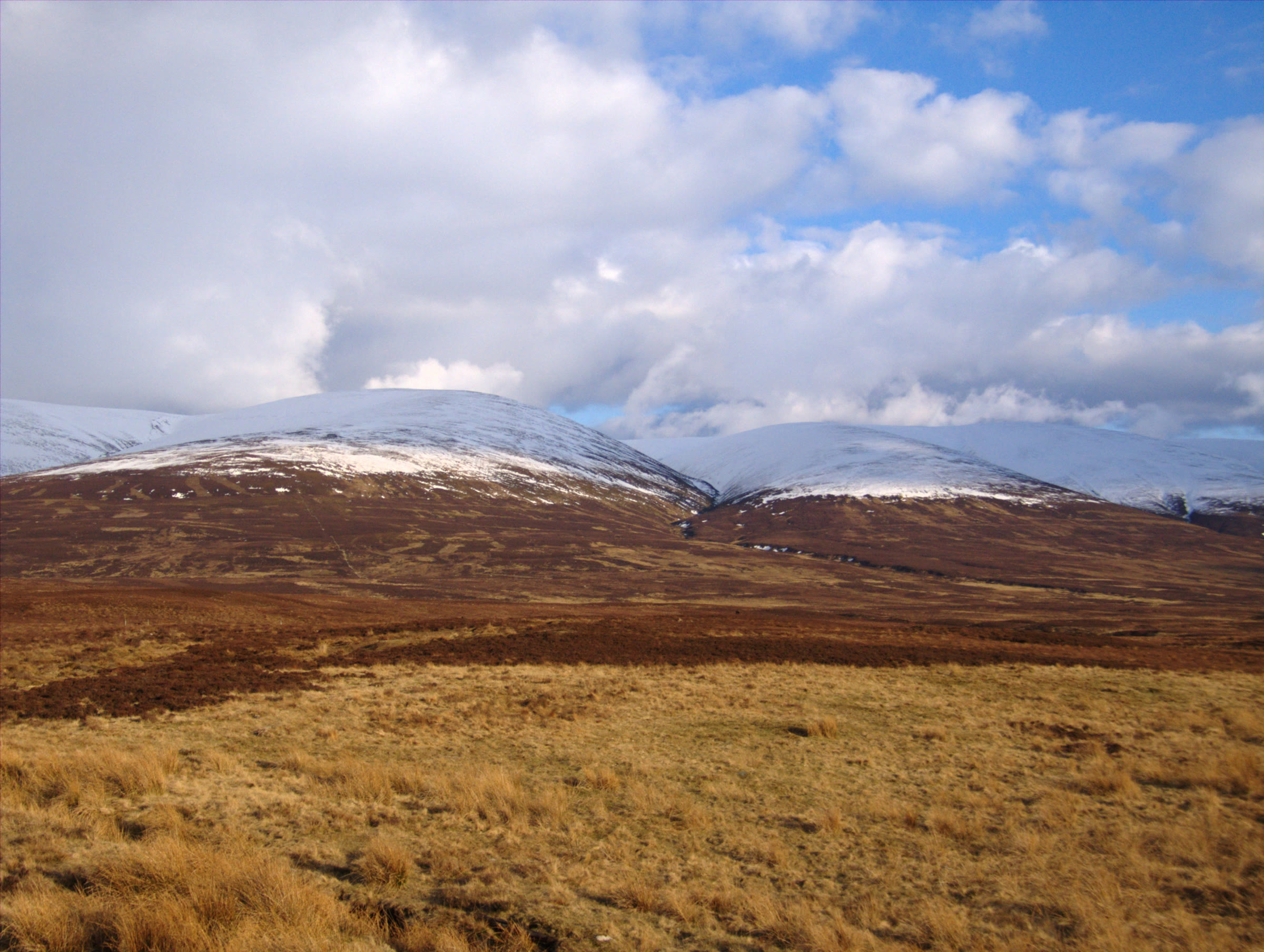The rounded, snow-capped top of Càrn na Caim above brown moorland and pale grass.
