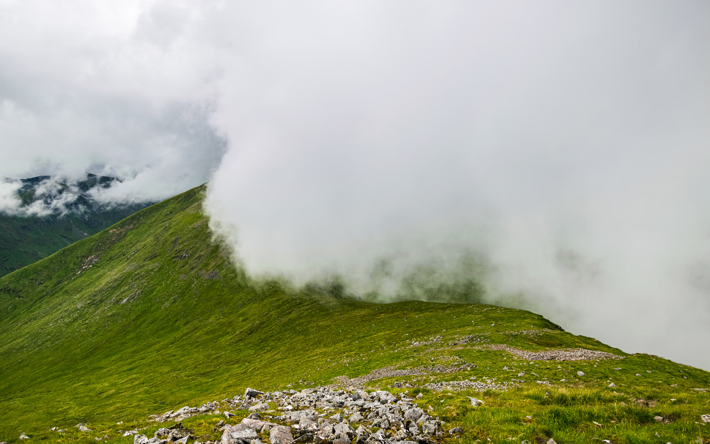 Low cloud rolling over a steep grassy ridge.