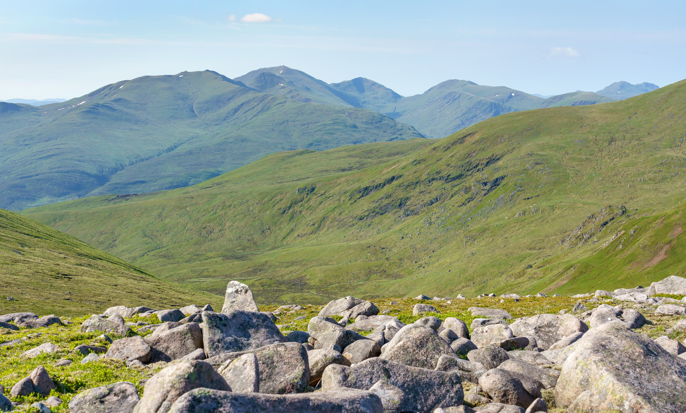 The Ben Lawers range across a green glen, with An Stuc, Ben Lawers, Beinn Ghlas and Meall Corranaich along the skyline, seen over summit boulders.