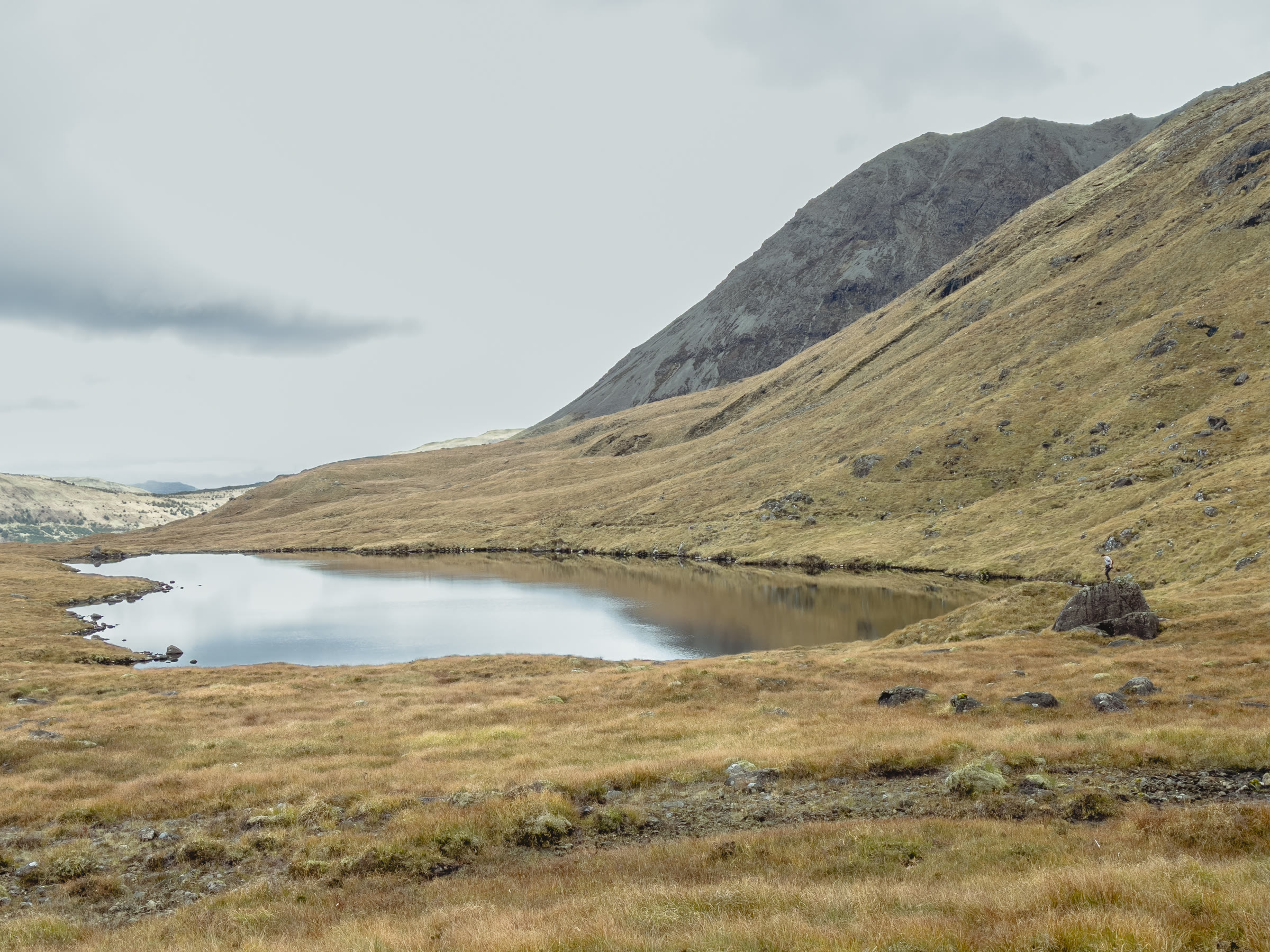 A lochan below tawny slopes below Sgùrr Alasdair, a rock ridge rising behind.