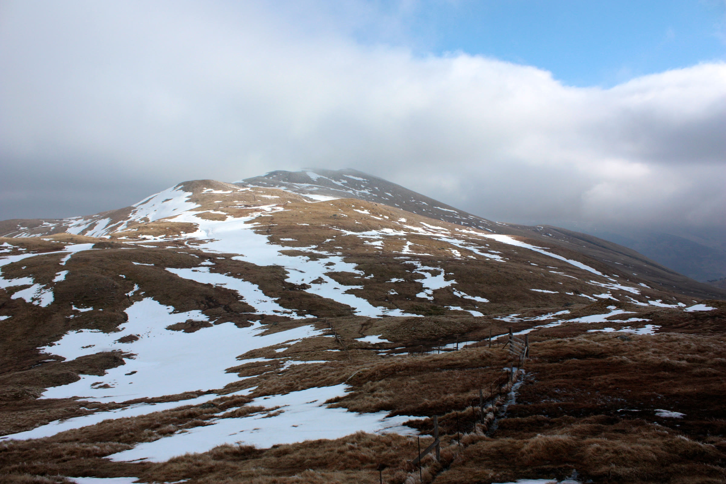 The rounded hill of Meall Greigh patched with snow, cloud brushing its top.