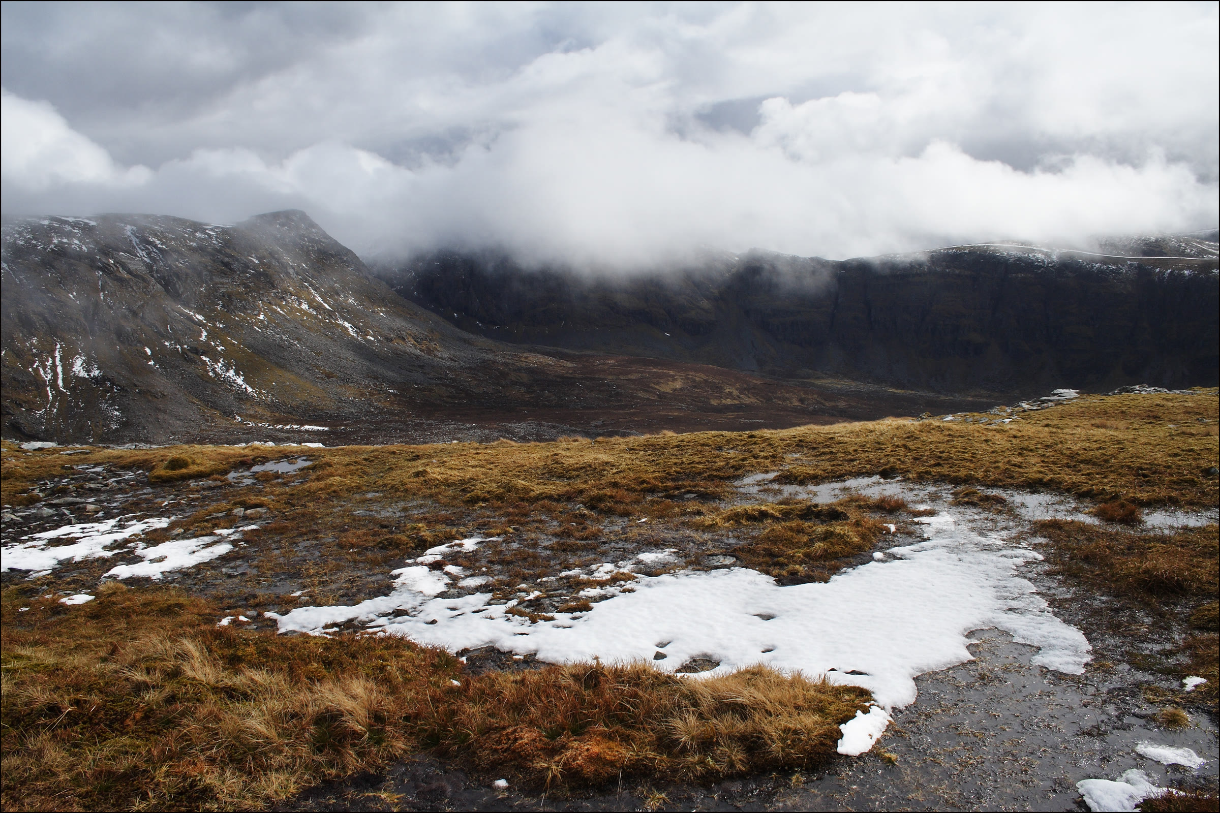 Meall nan Ceapraichean dusted with snow under low cloud, across a moor with melting drifts.