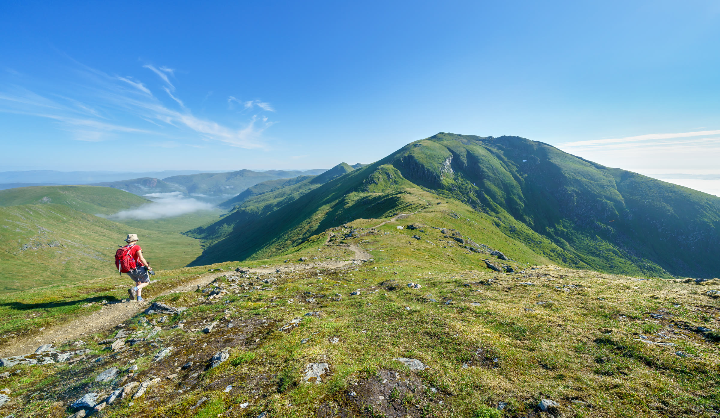 A walker on the path from the top of Beinn Ghlas towards Ben Lawers, mist lying in the glen beyond.