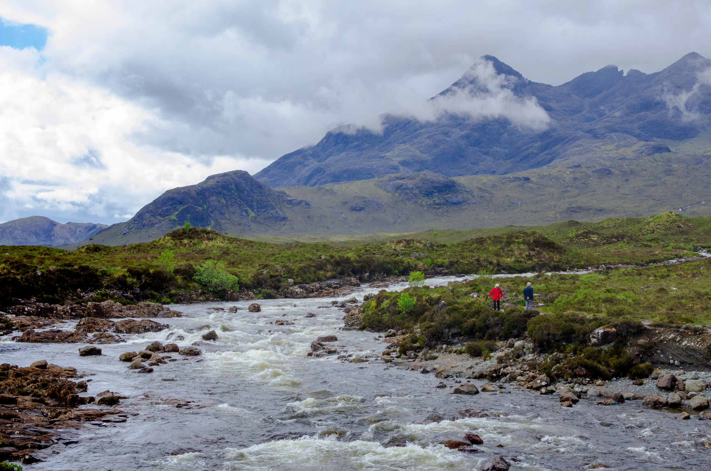 The river at Sligachan below Sgùrr nan Gillean, Am Basteir and the Basteir Tooth, two walkers small on the far bank.