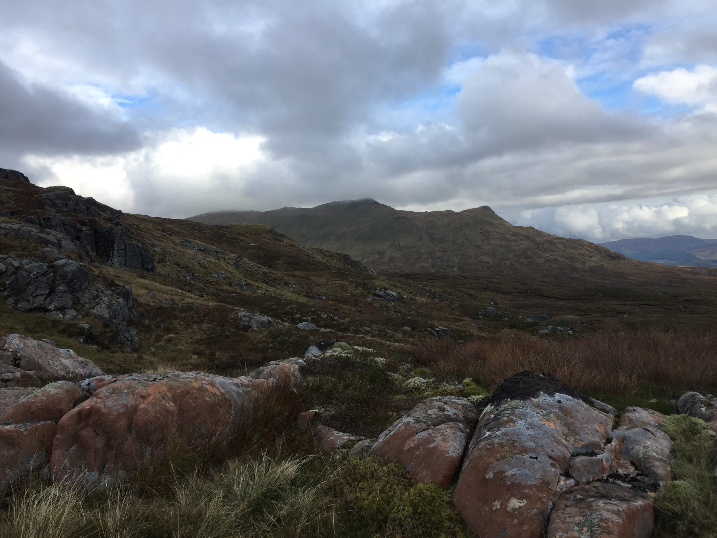 The craggy top of Sgiath Chùil across the glen, with lichen-covered boulders in front.