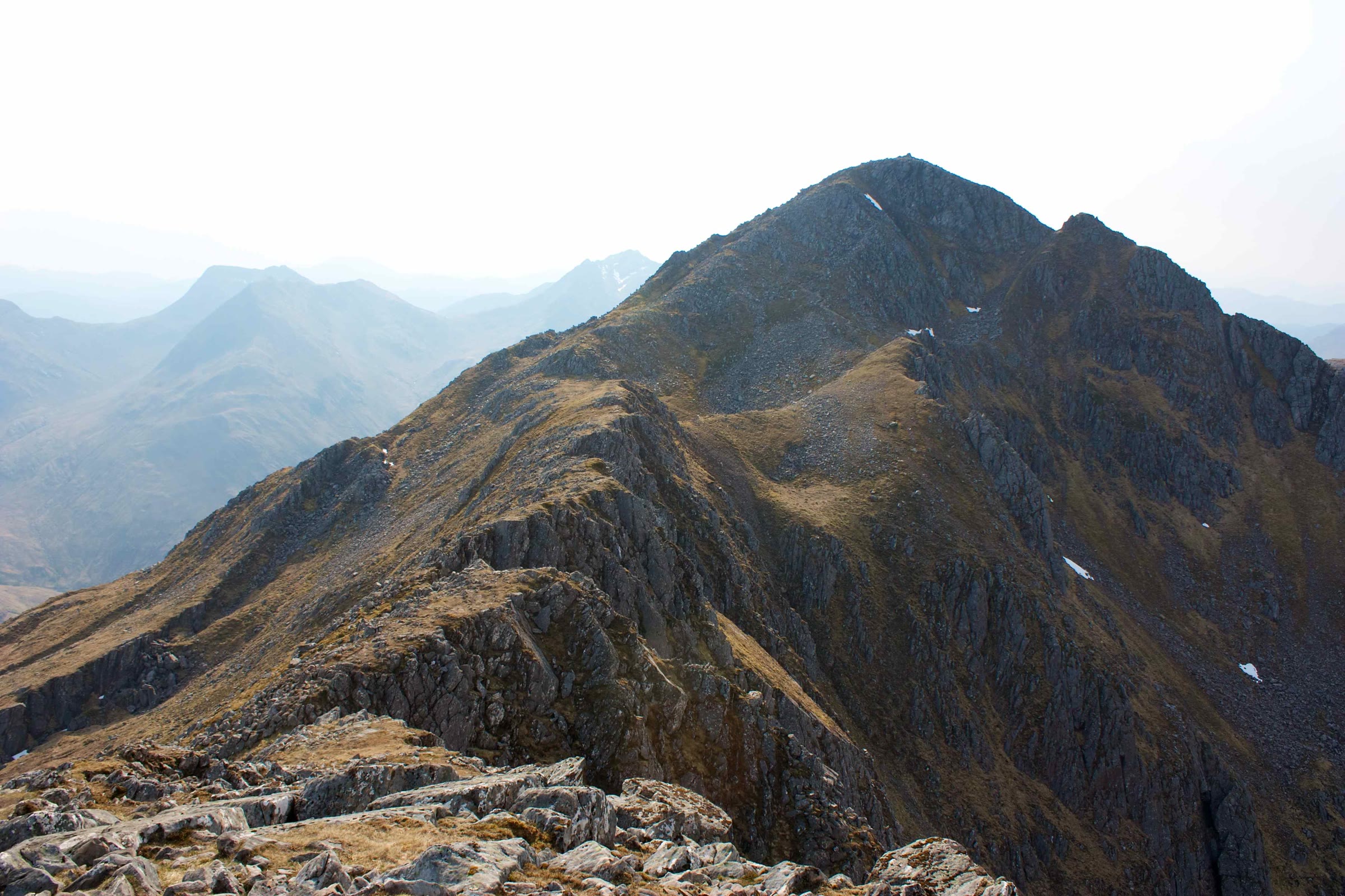 The rocky peak of Sgùrr na Ciste Duibhe at the end of its ridge, hazy hills beyond.