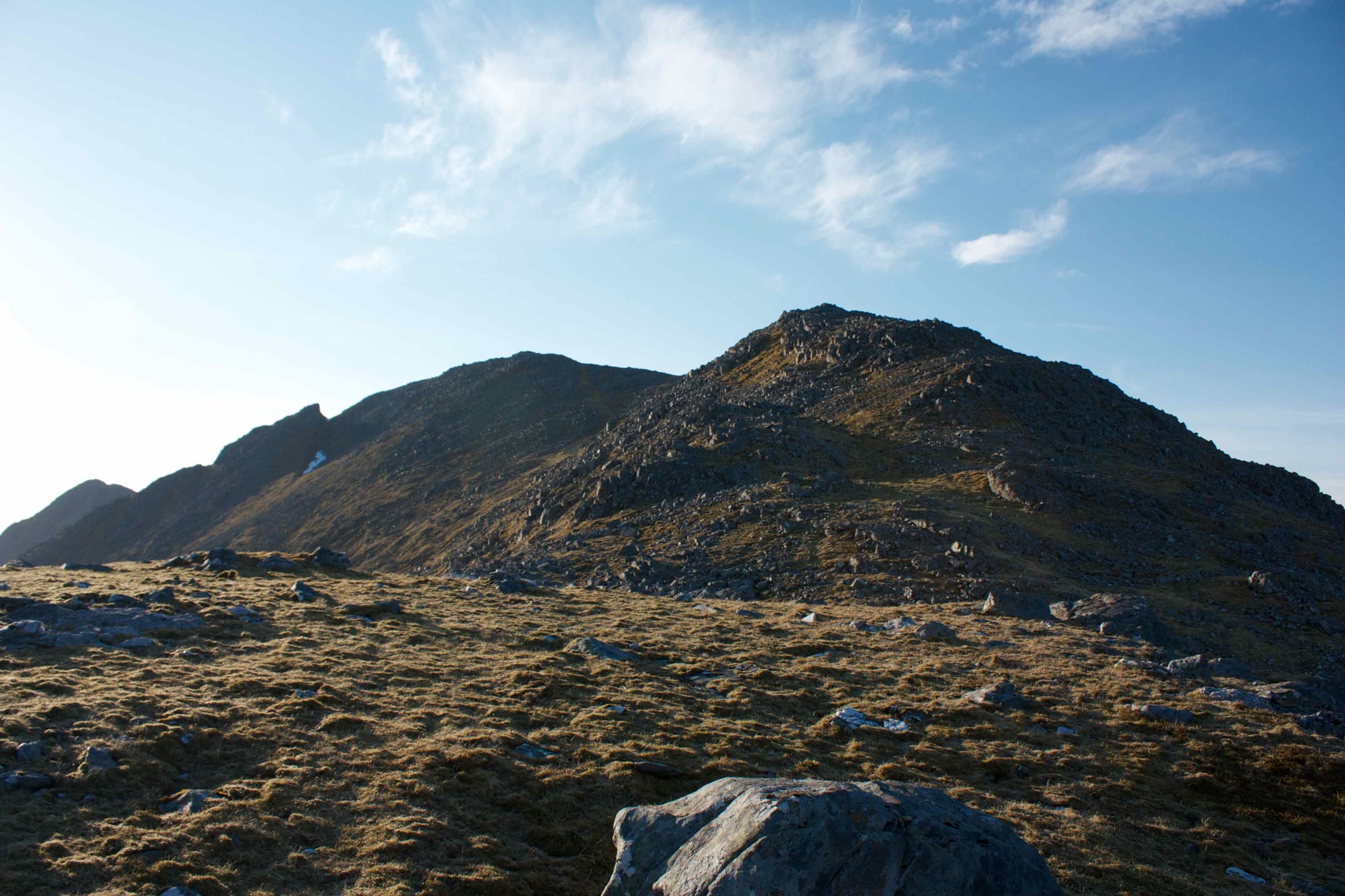 Sgùrr na Ciste Duibhe from a grassy shoulder under a blue sky.