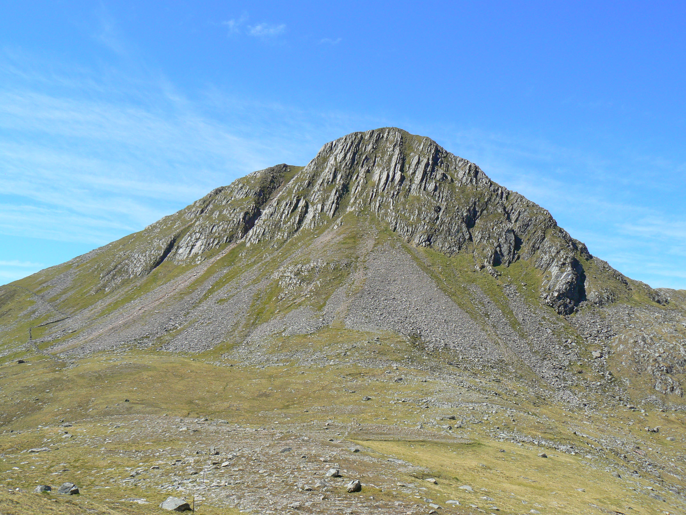 The rocky face of Sgùrr na Sgìne above grass and scree, under a blue sky.