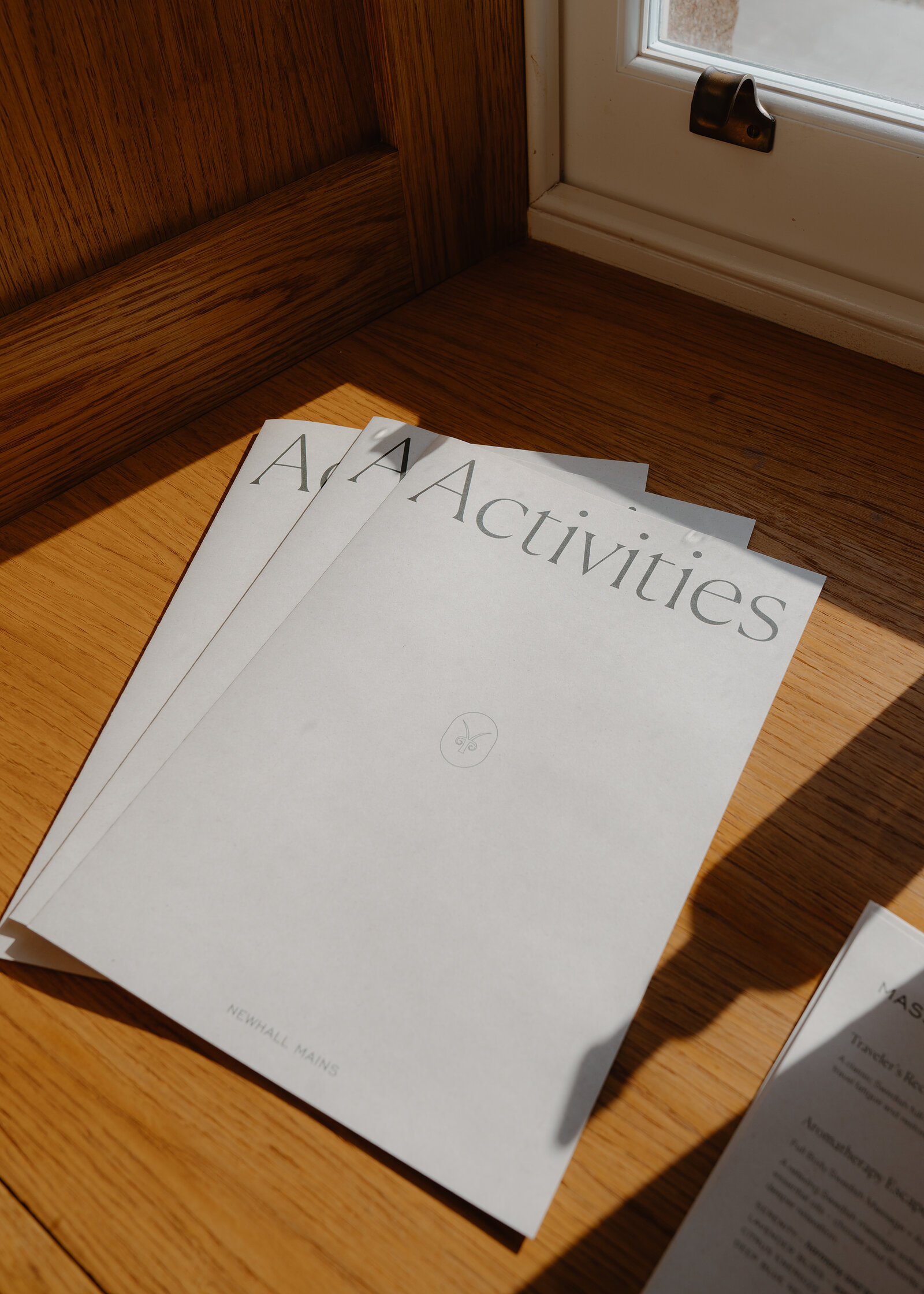 Two booklets titled Activities, printed for Newhall Mains, lie on a sunlit wooden windowsill.