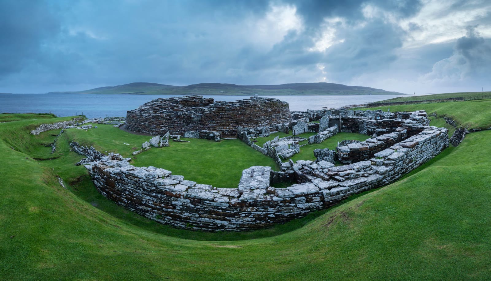 The Broch of Gurness and the stone village round it on the shore of Eynhallow Sound, Rousay across the water.