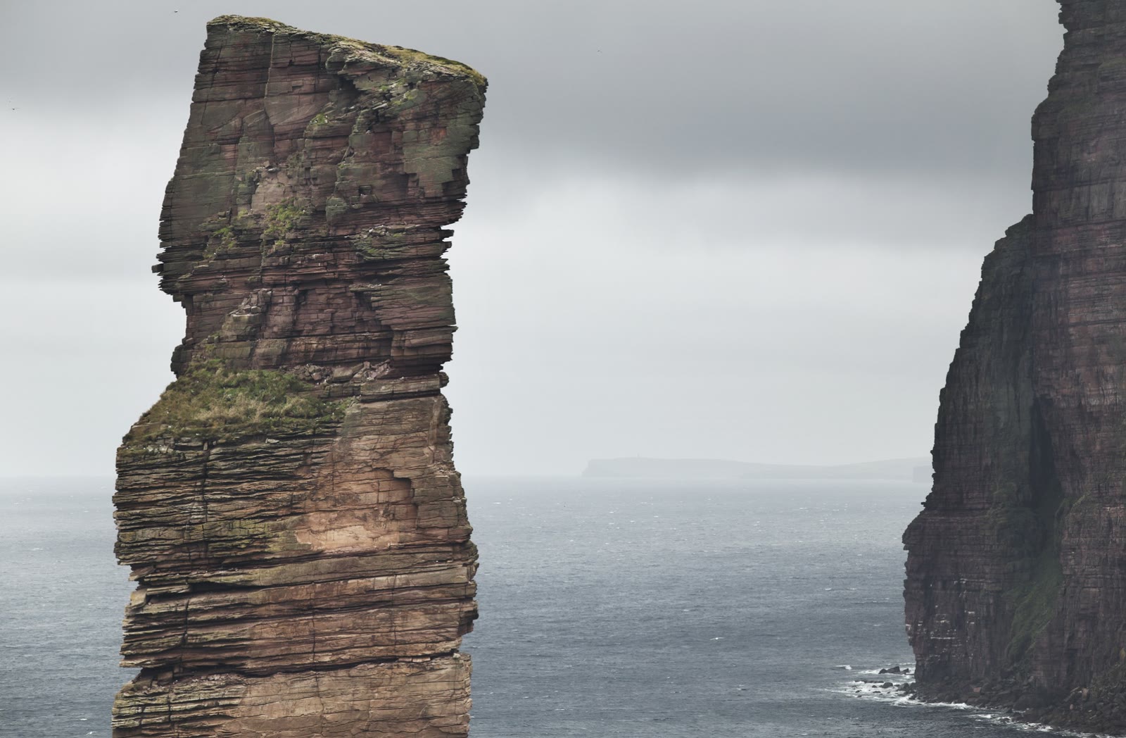 The Old Man of Hoy, a tall red sandstone sea stack, standing off the cliffs of Hoy under a grey sky.