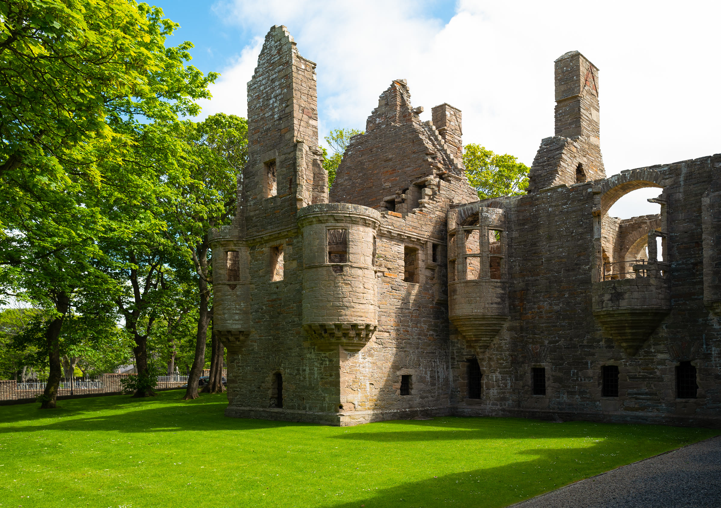 The Earl's Palace in Kirkwall, its roofless walls with corbelled turrets, oriel windows and tall chimneys standing on a green lawn among trees, Orkney.