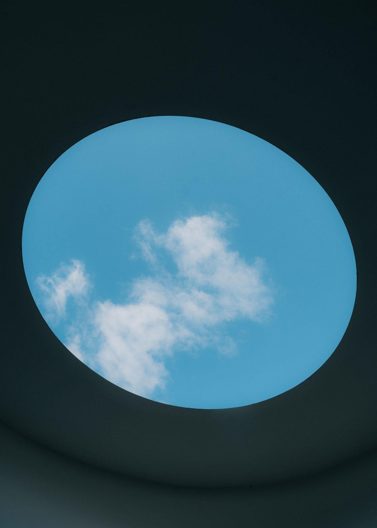 The oval oculus in the chamber ceiling frames blue sky and a drifting white cloud against the dark surrounding ceiling.