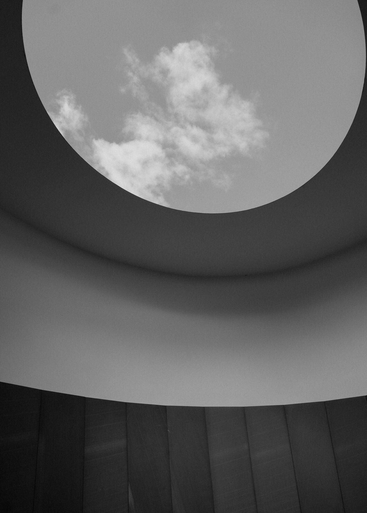 In black and white, looking up from the chamber at the oculus and its cloud, above the curved ceiling and panelled wall.