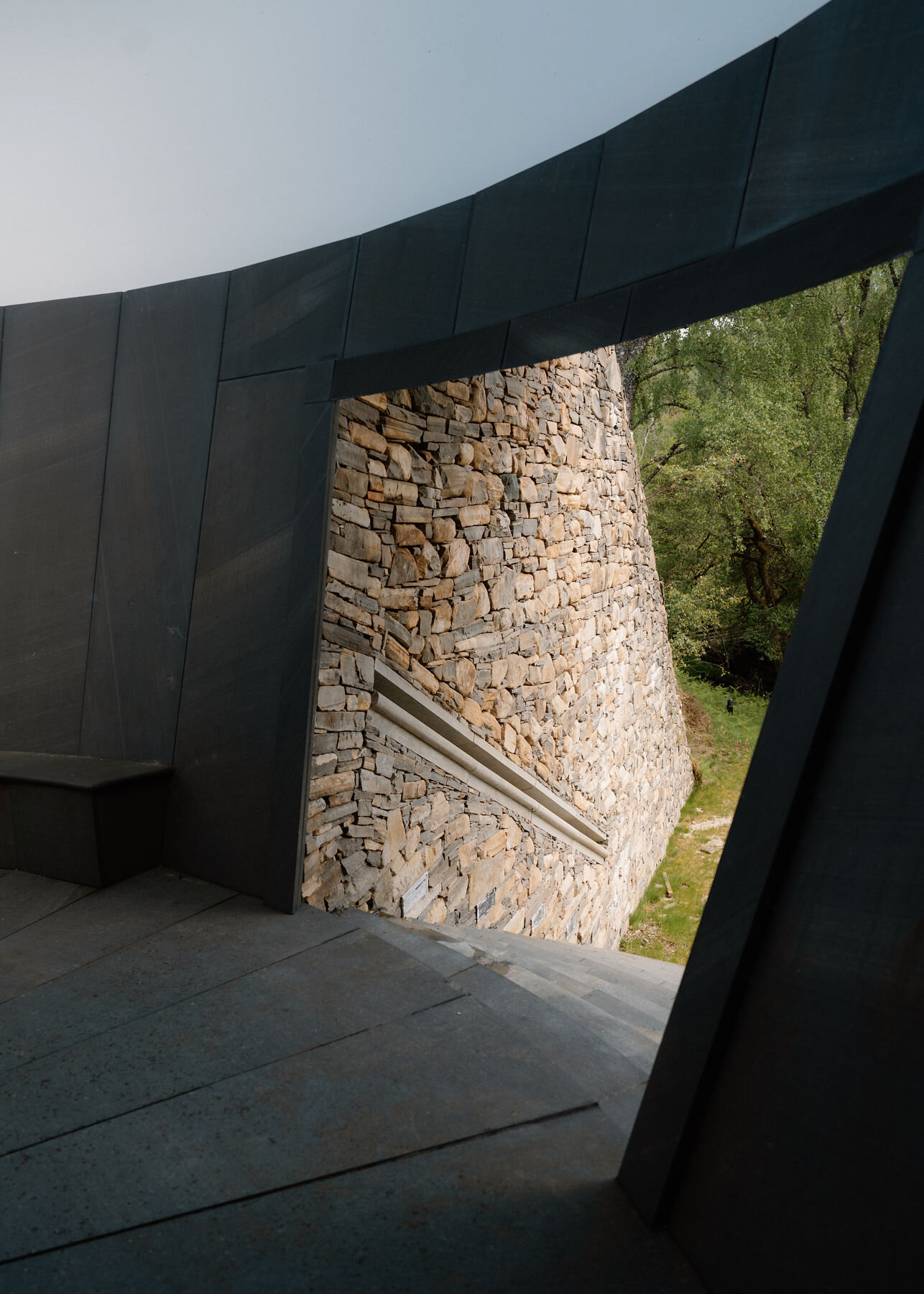 From inside the chamber doorway, steps lead down past the drystone wall and its handrail to grass and birch trees.