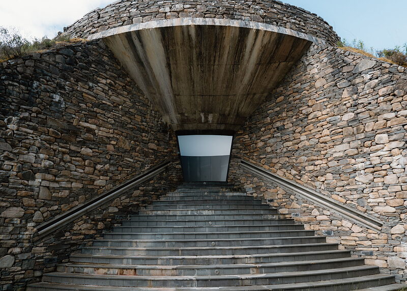 A broad head-on view of the skyspace steps climbing to the doorway under the concrete canopy, with heather on the walls' tops.