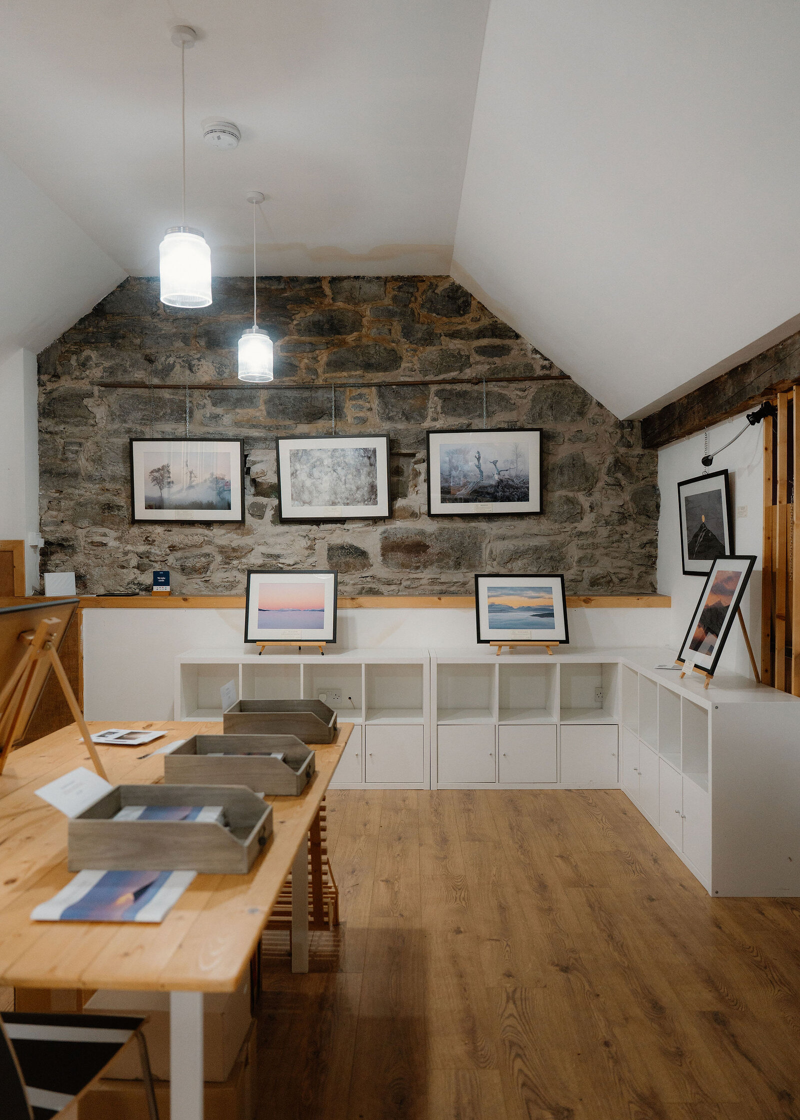 The gallery interior from slightly further back, with trays of cards on the pine table and more of the wooden floor.