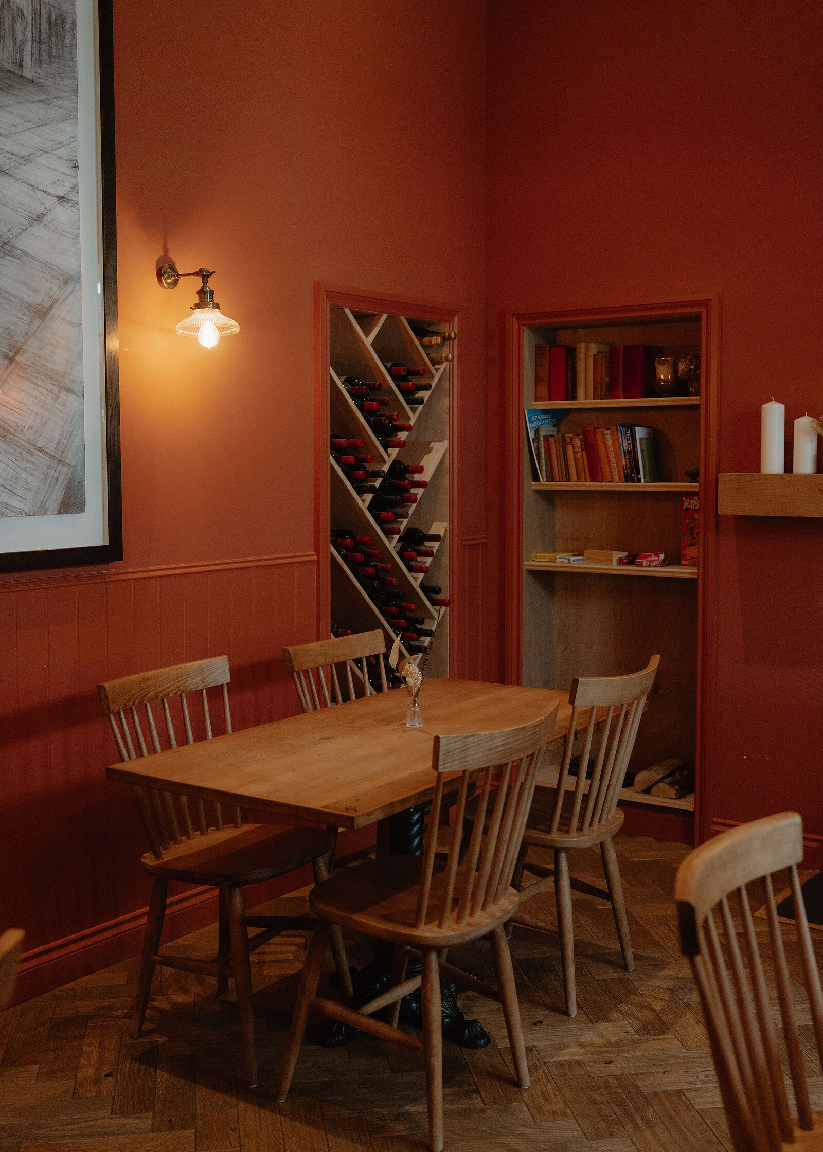 A tighter view of the table and chairs by the wine rack and bookshelf, with candles on a mantel at the right.