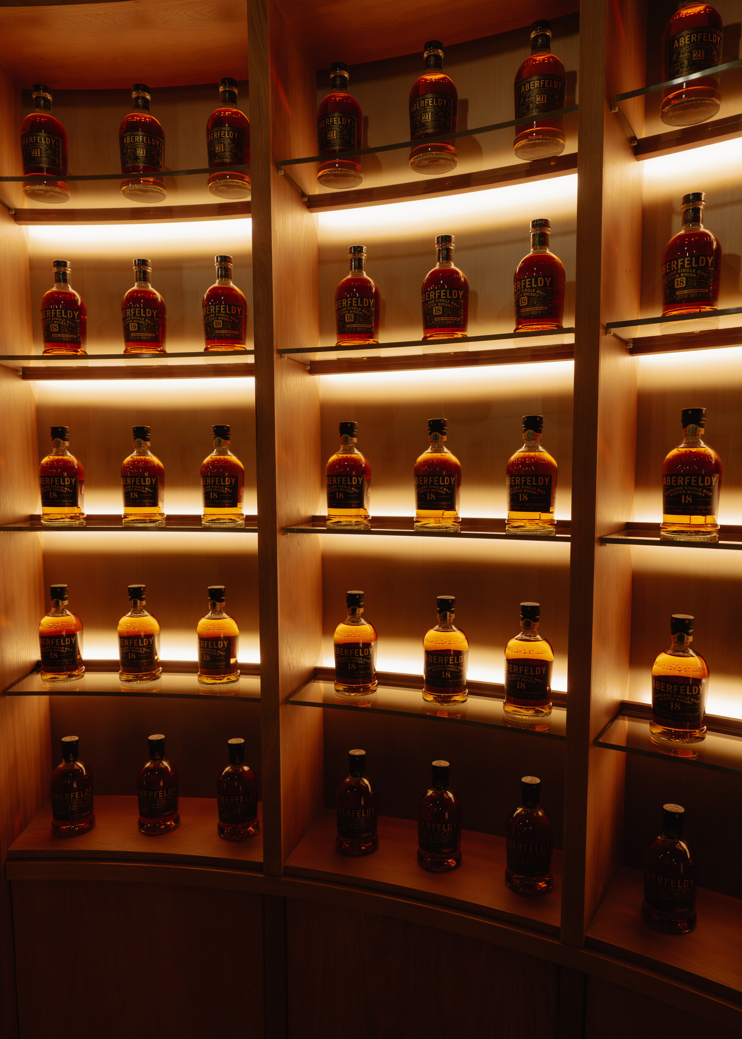 Bottles of Aberfeldy standing in rows of warm backlit alcoves in the tasting room.