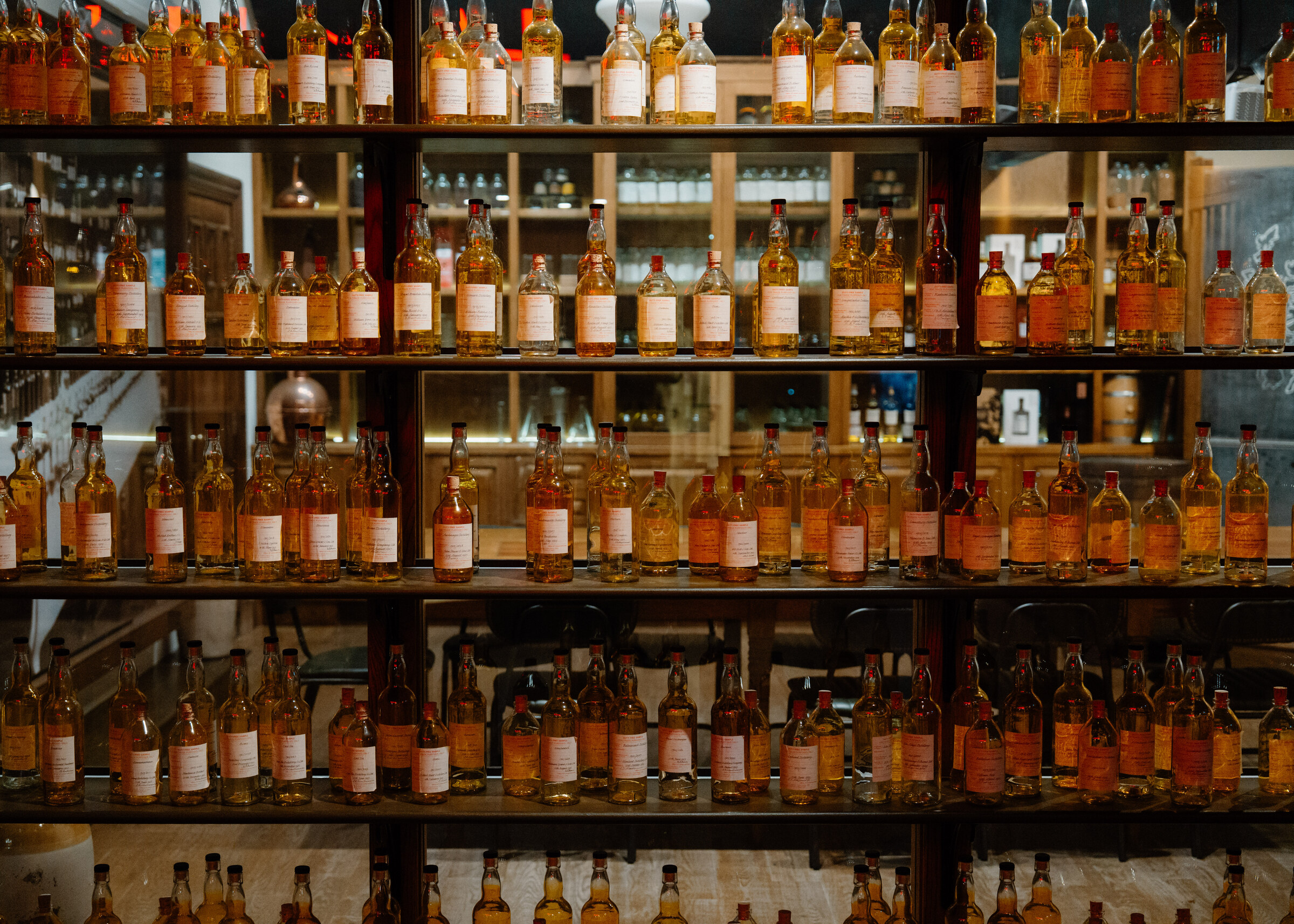 Shelf upon shelf of whisky bottles in amber rows, lit from behind.