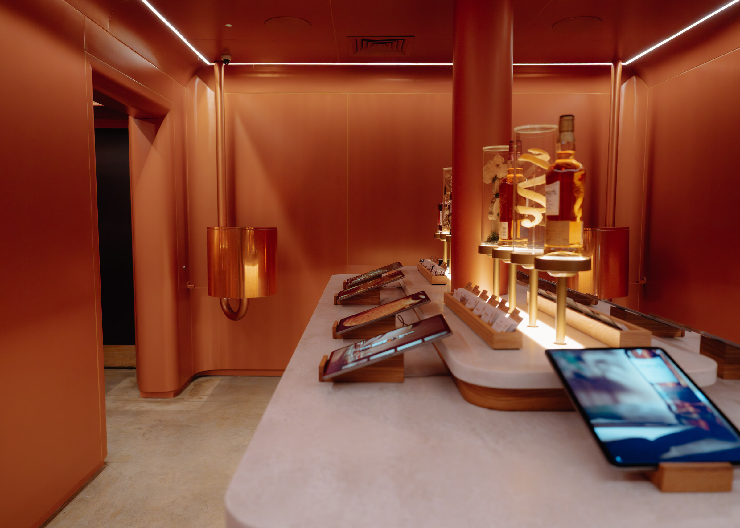 A copper-toned room of white counters set with tablets and bottles on lit stands, part of the distillery's experience rooms.
