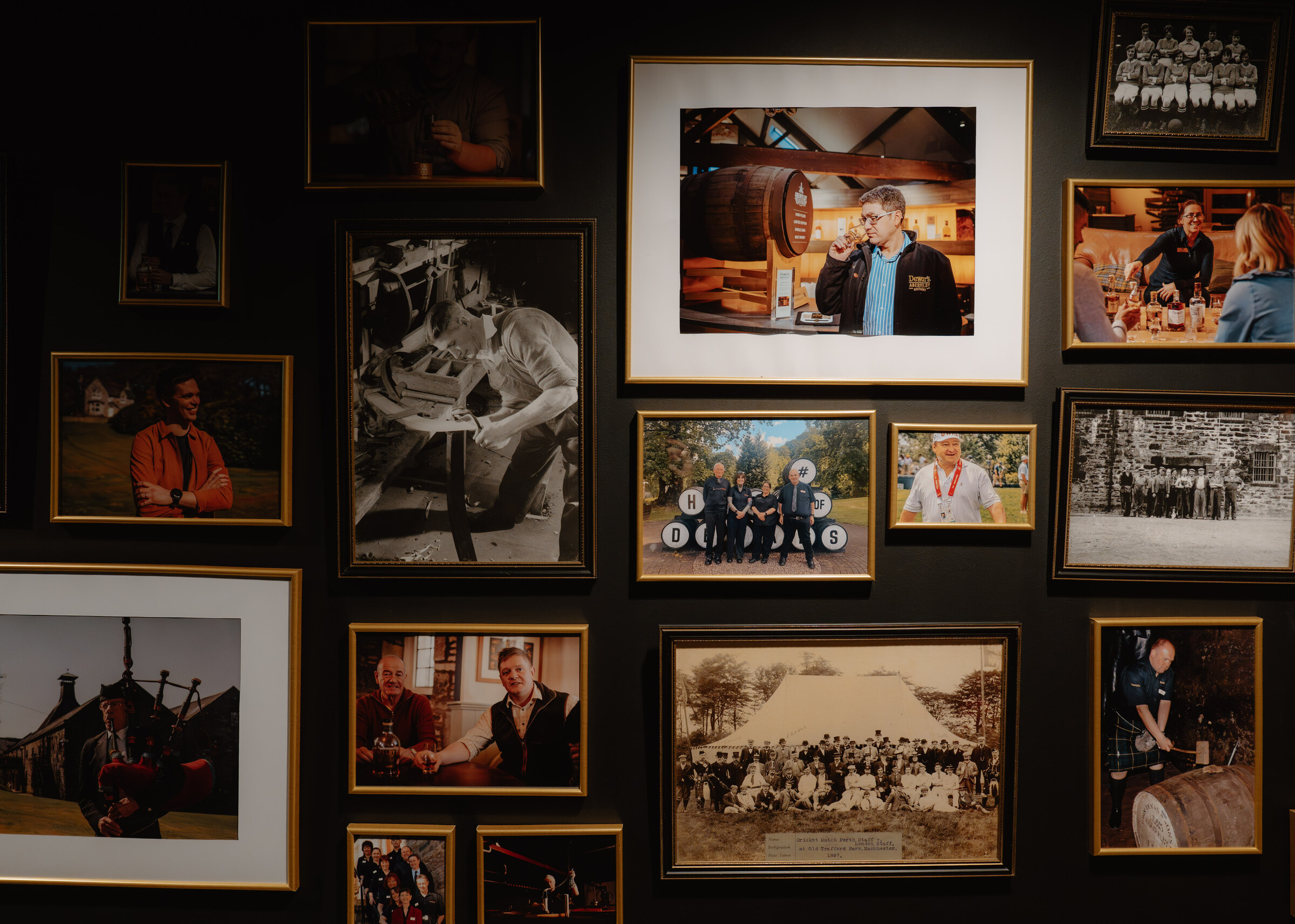 A wall of framed photographs of distillery workers and their families, old and new, black-and-white and colour.