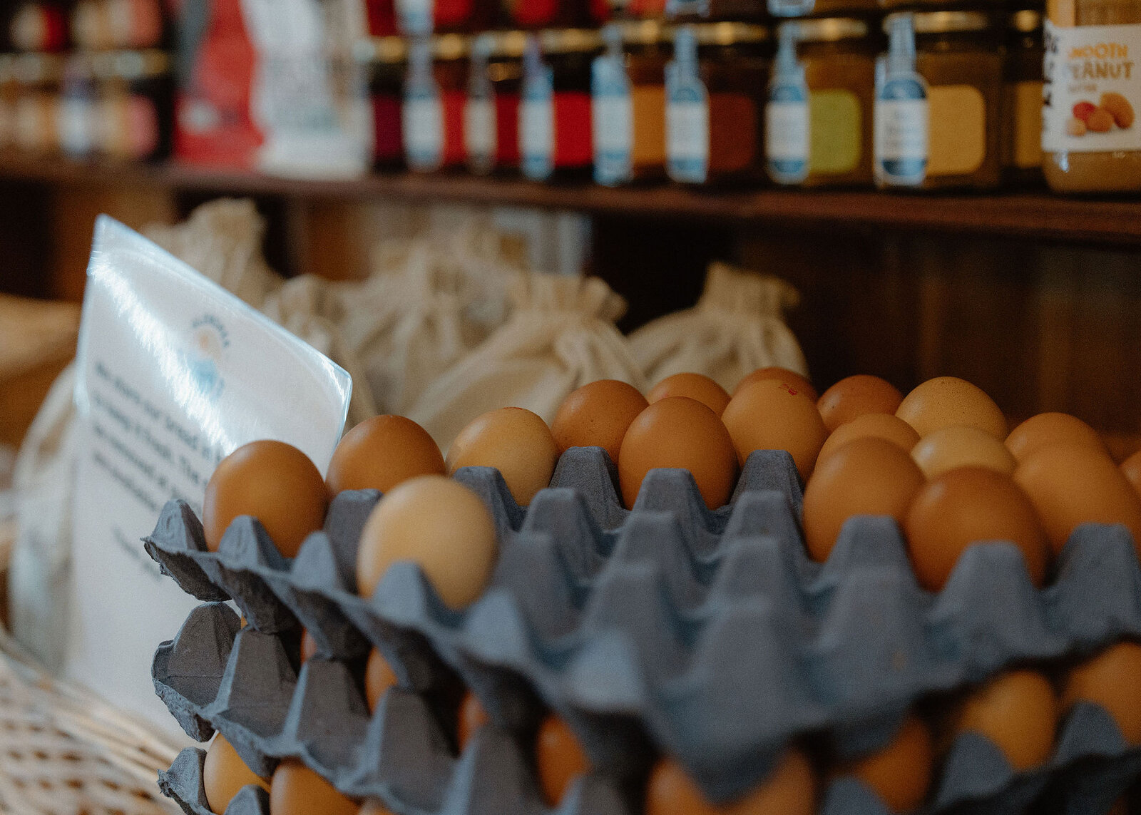 Trays of brown eggs for sale on a shelf in the cafe's deli, jars of jam and sauces on the shelf above.