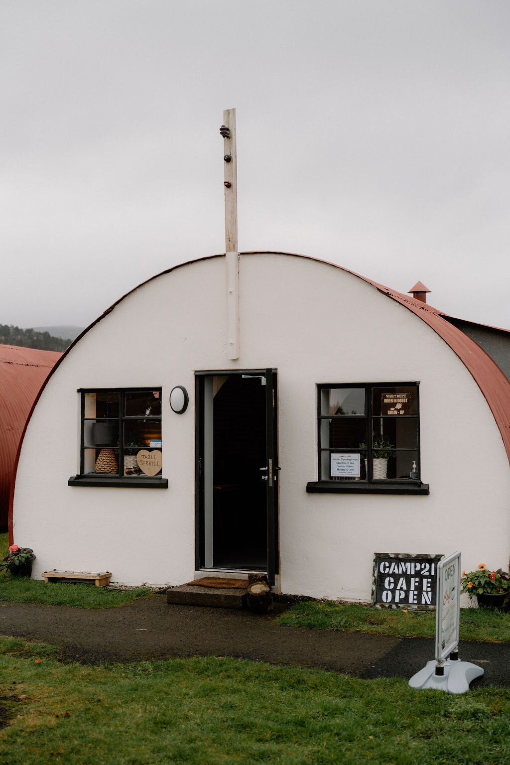A white Nissen hut cafe with a red roof advertises itself open beside a sandwich board.
