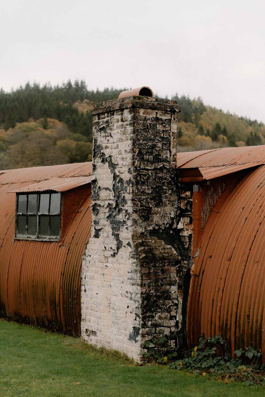 A whitewashed chimney rises from a rust-streaked Nissen hut roof beside autumn trees.