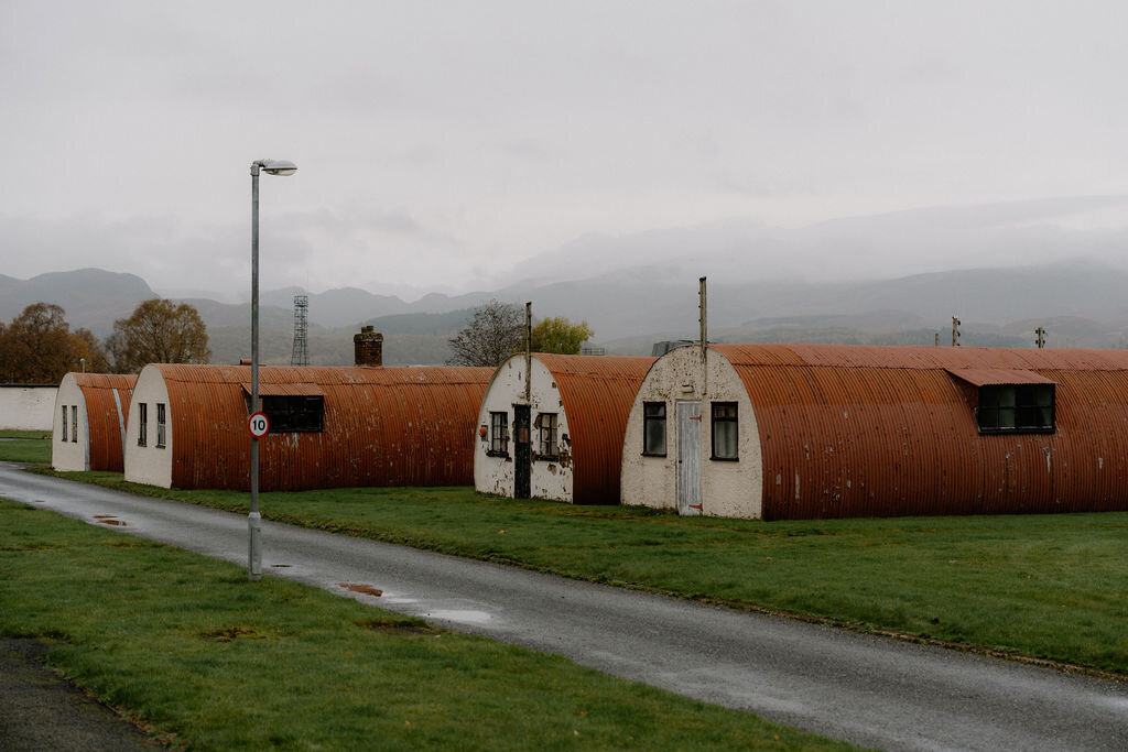 Two corrugated Nissen-hut chalets with painted doors sit on the grass beside a street lamp.